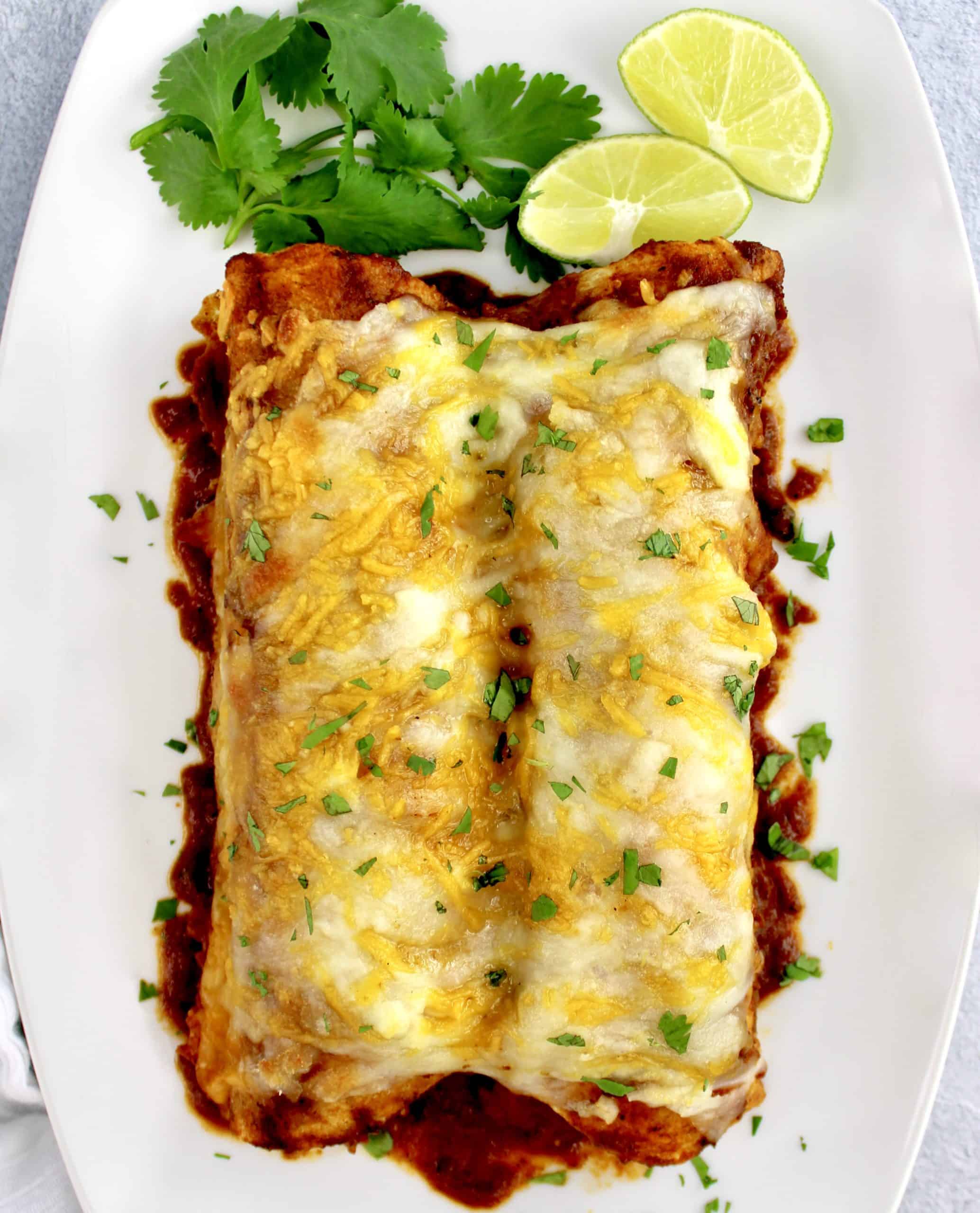 overhead view of 2 Keto Chicken Enchiladas on white plate with lime on side