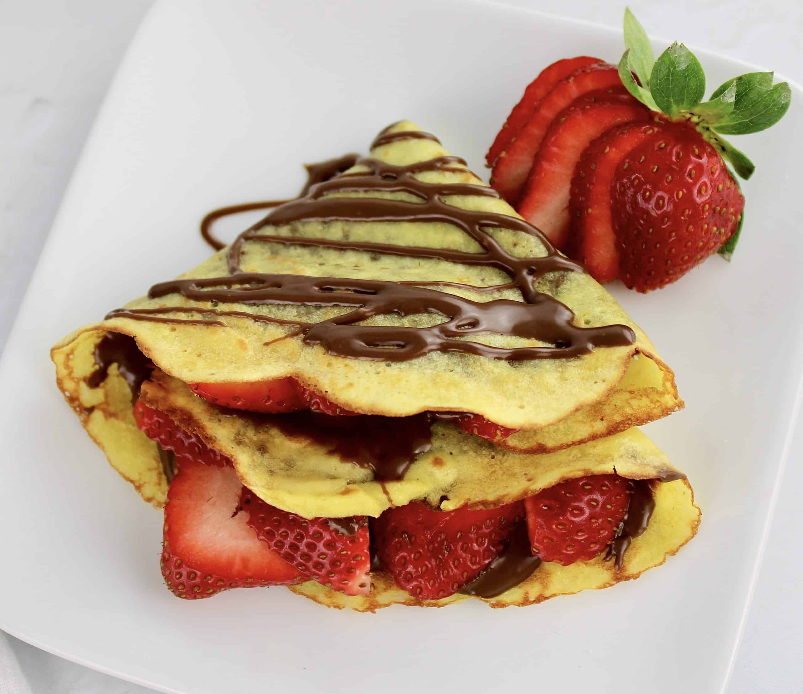 crepe with nutella and cut strawberries on white plate
