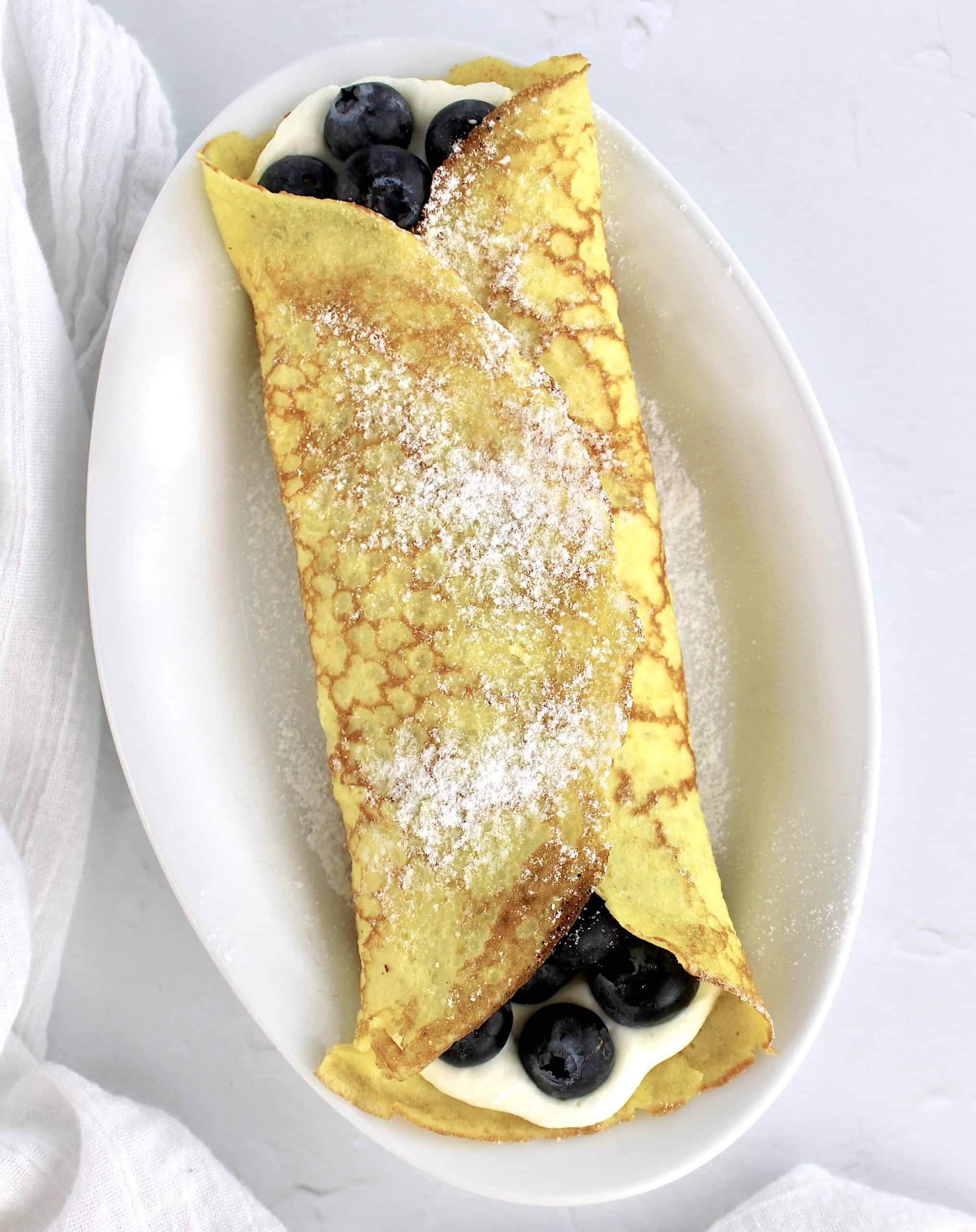 crepes with whip cream and blueberries on white plate