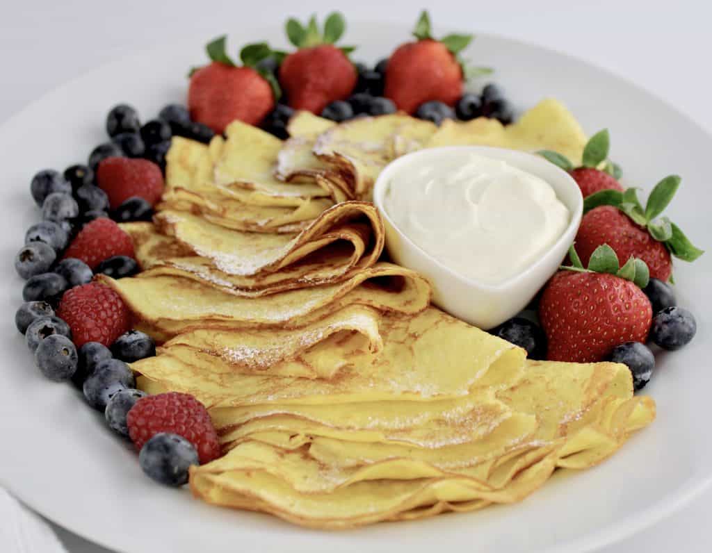 crepes on white plate with berries and whip cream