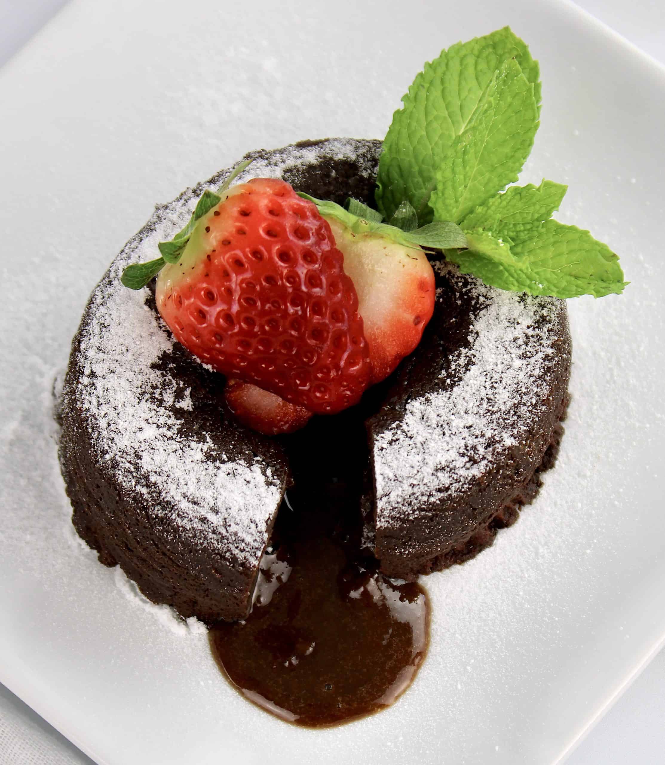 overhead view of chocolate lava cake on white plate with strawberry and mint on top