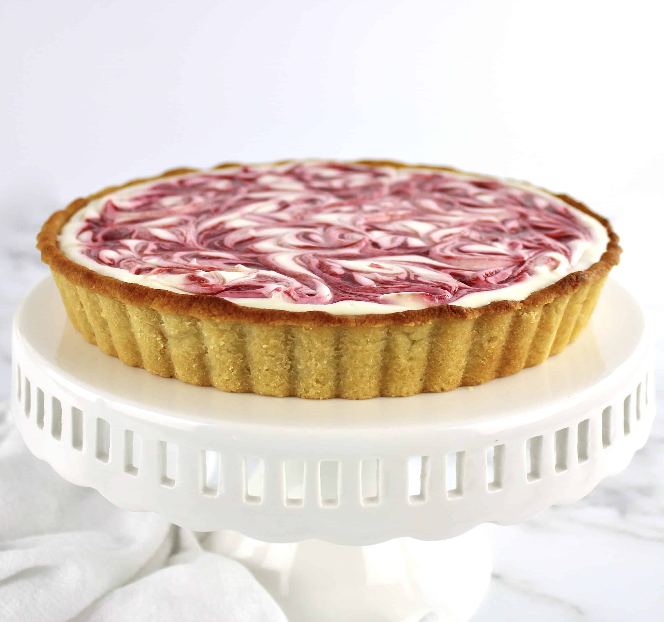 side view of Keto White Chocolate Raspberry Cheesecake on white cake stand
