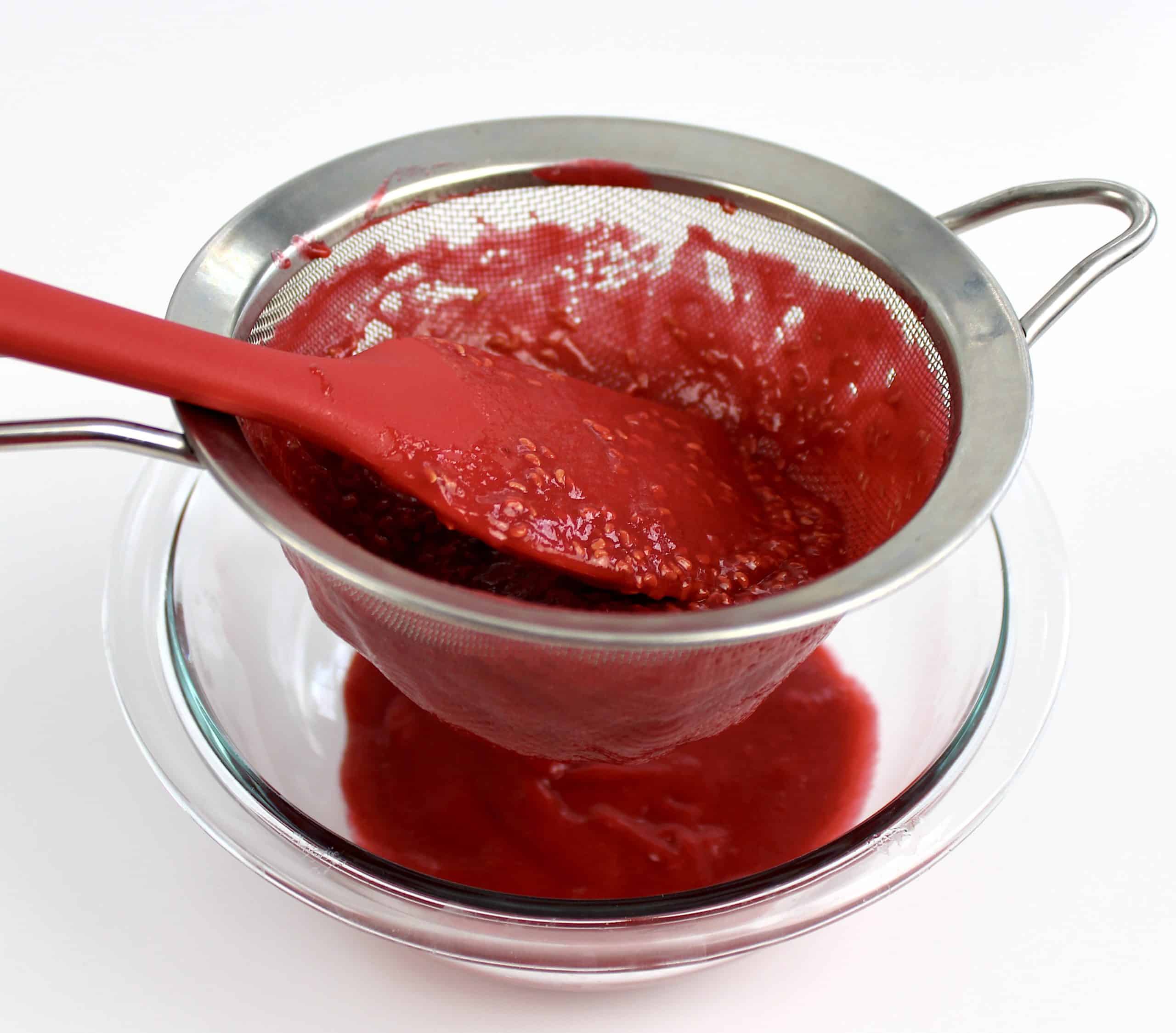 raspberry sauce being strained in sieve