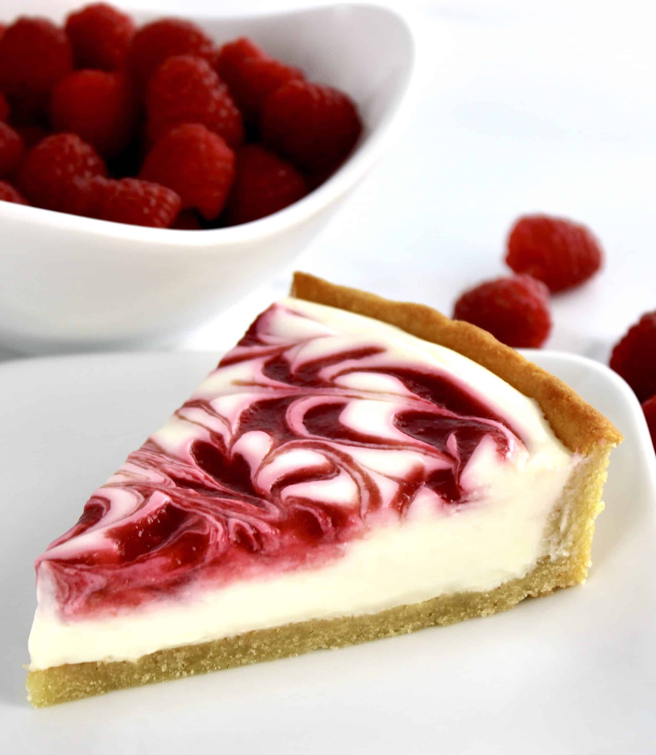 slice of Keto White Chocolate Raspberry Cheesecake on white plate with raspberries in background