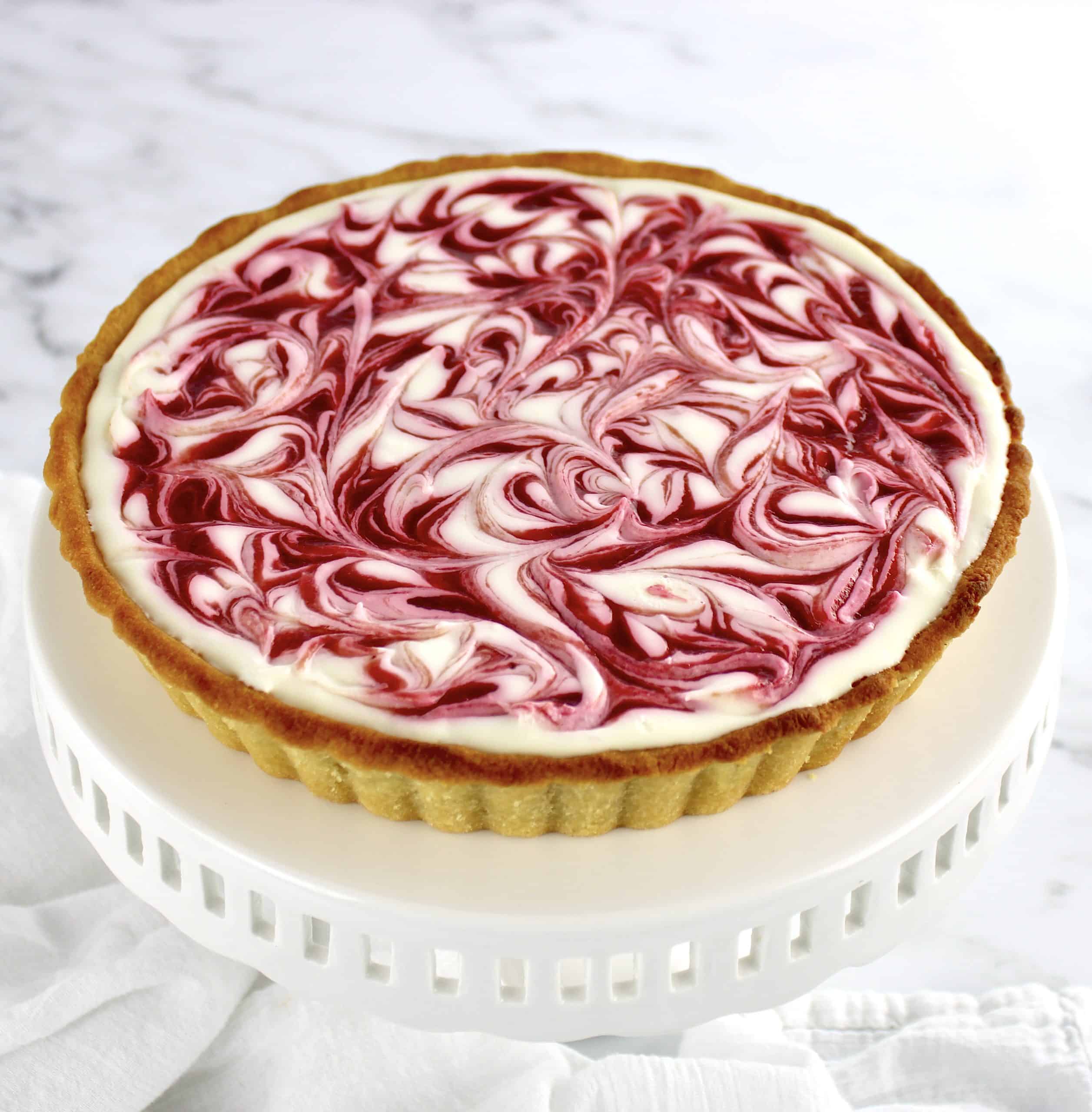 Keto White Chocolate Raspberry Cheesecake on white cake stand