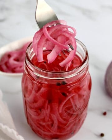 Pickled Red Onions being held up out of jar with a fork