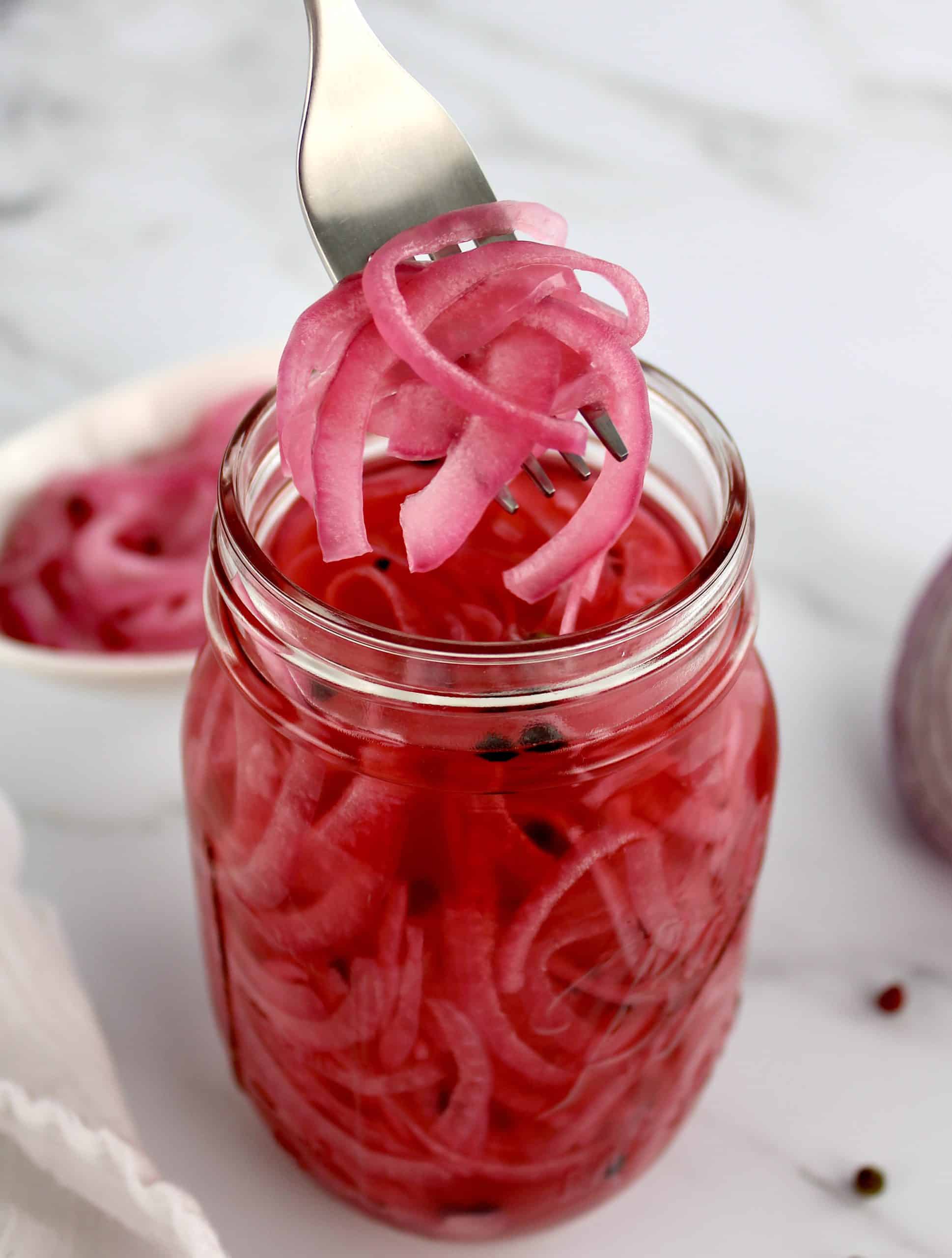 Pickled Red Onions being held up out of jar with a fork