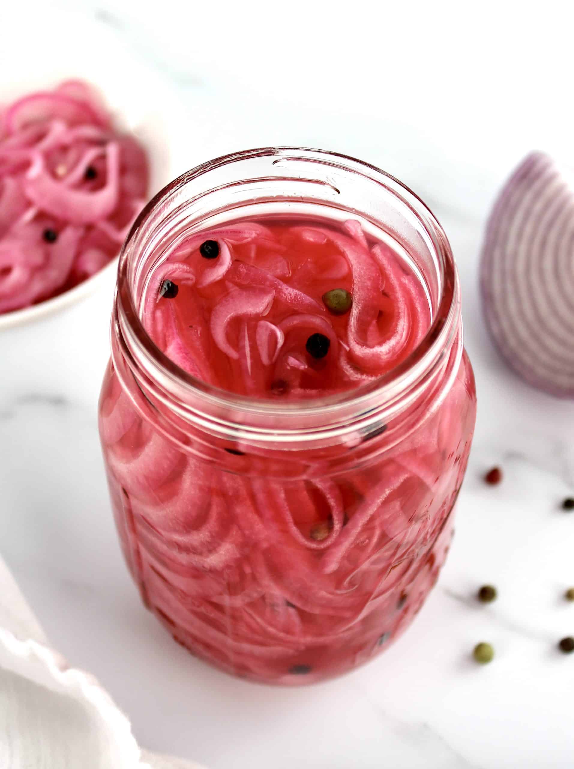 Pickled Red Onions in open mason jar with peppercorns