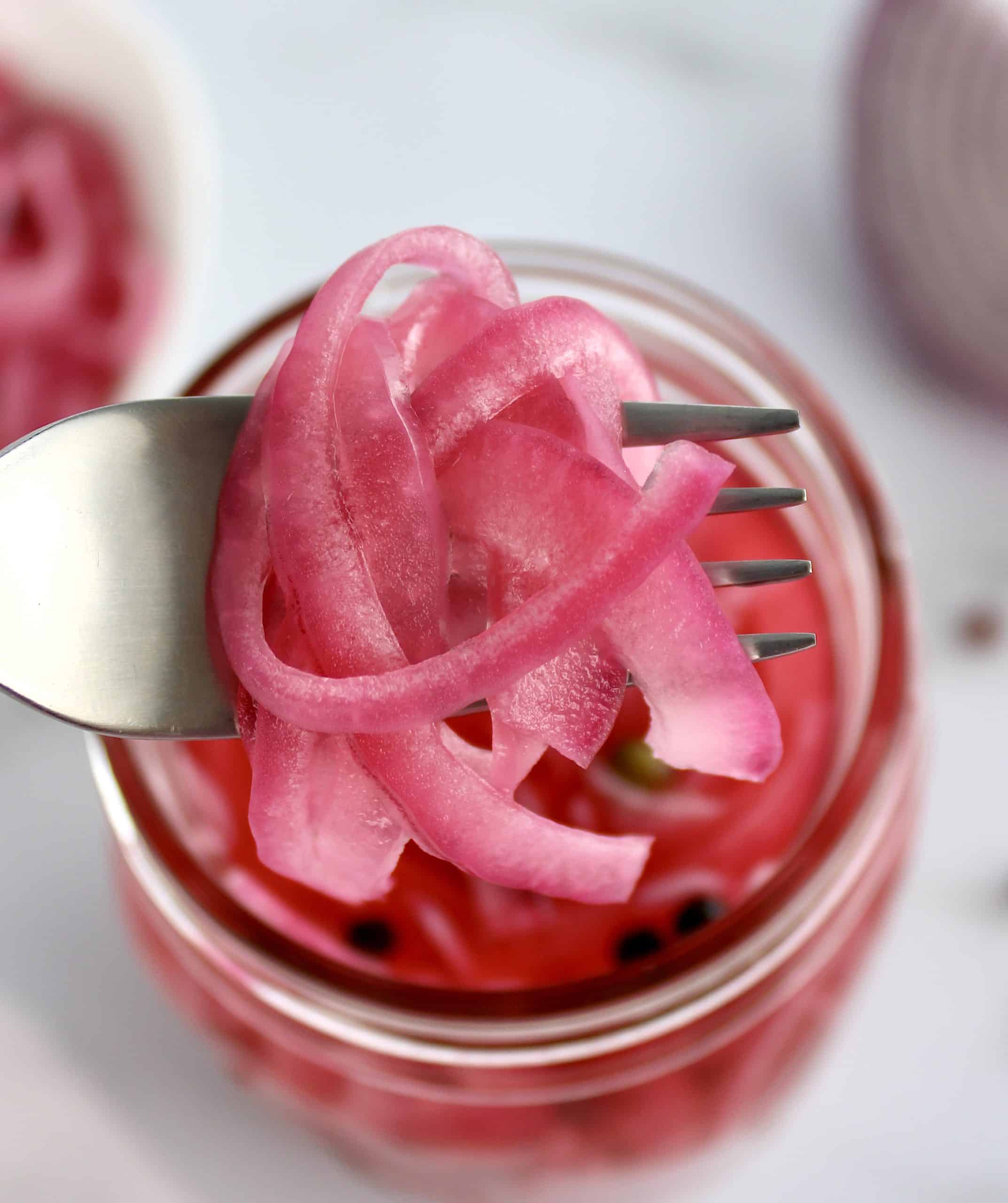 Pickled Red Onions being held up with fork out of jar