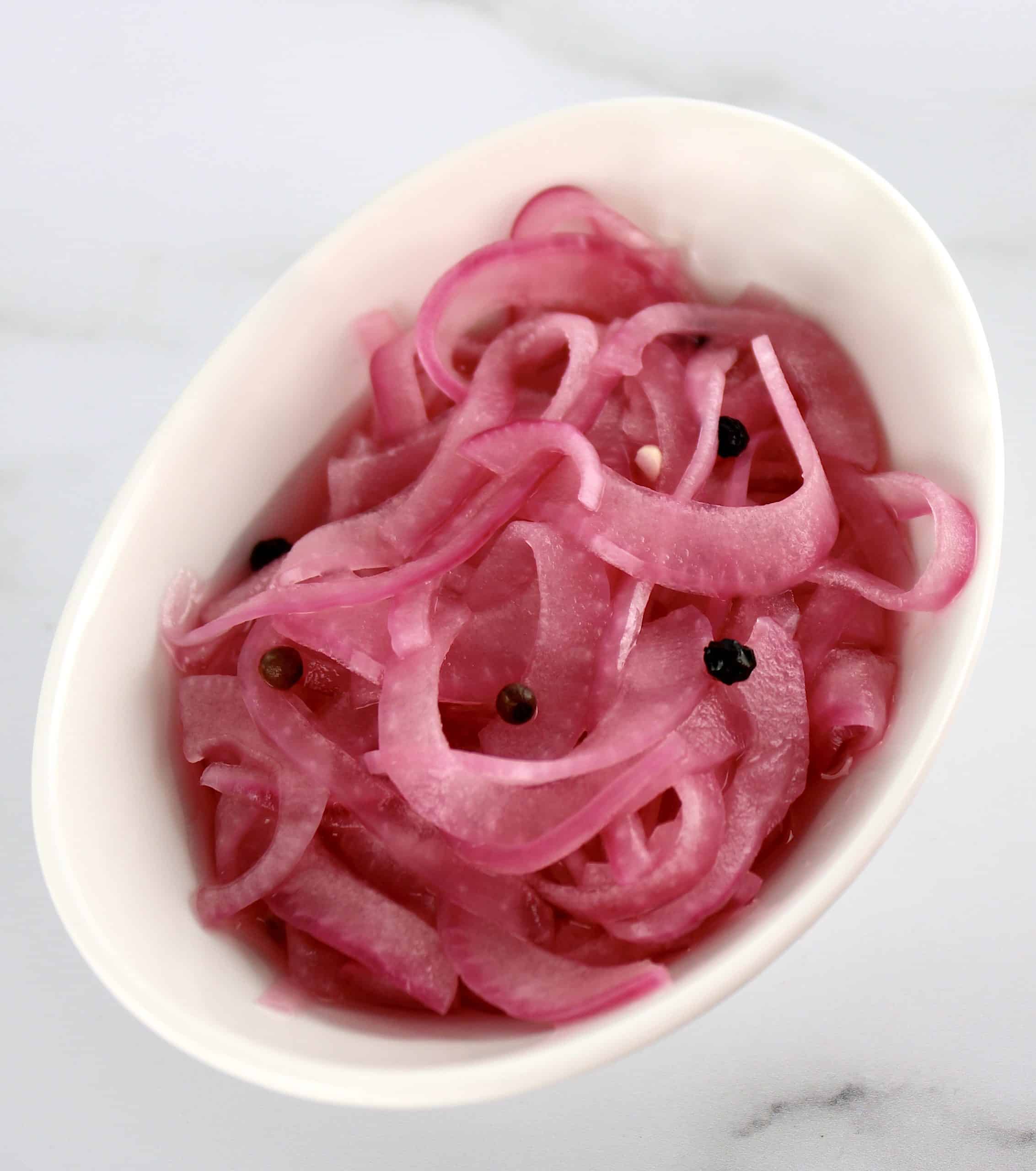 Pickled Red Onions in white bowl with peppercorns
