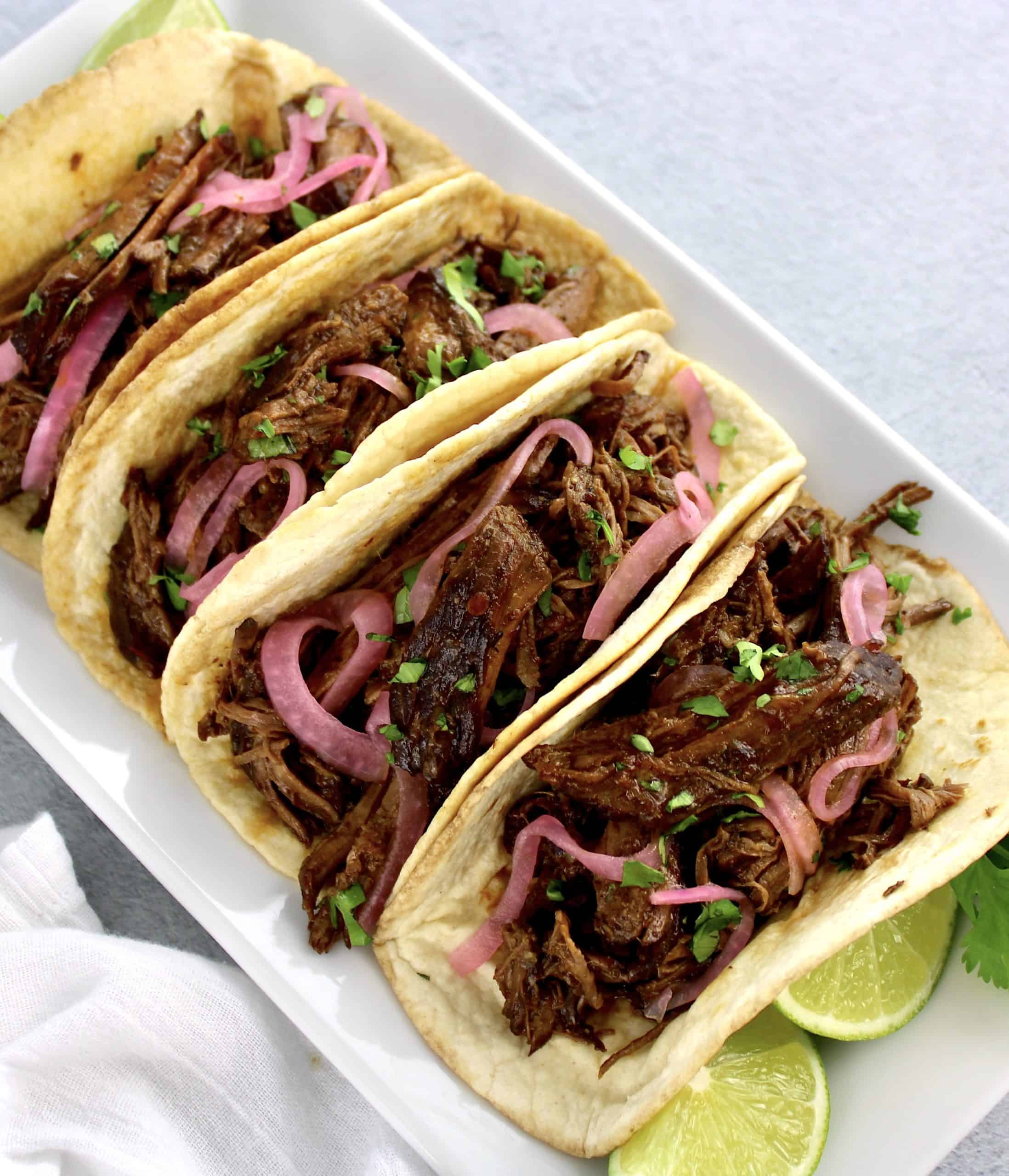 Slow Cooker Beef Barbacoa in tortillas with lime slices on side