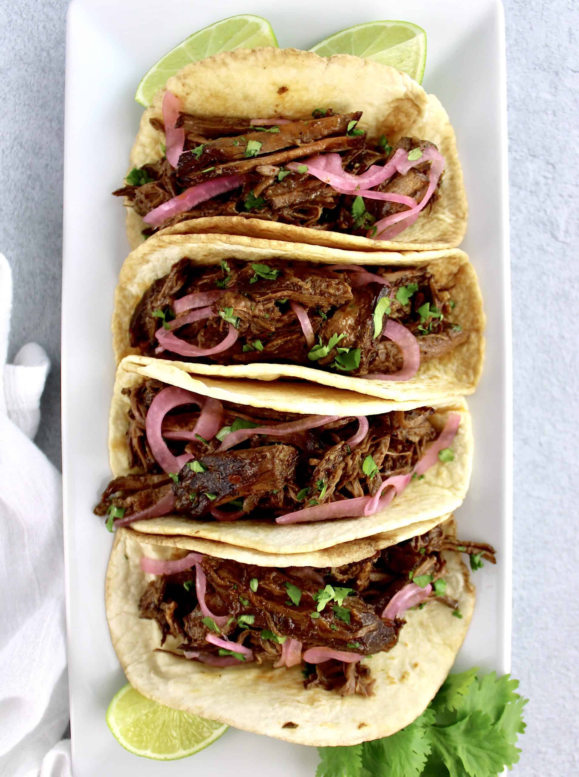Slow Cooker Beef Barbacoa in tortillas with lime slices on side