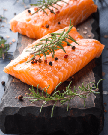 2 pieces of salmon on black slate with rosemary and peppercorns