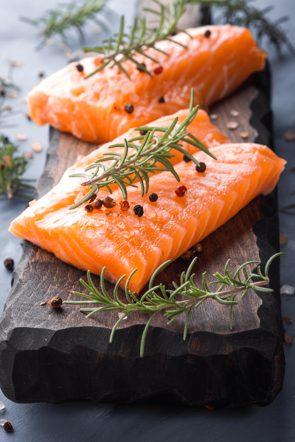 2 pieces of salmon on black slate with rosemary and peppercorns