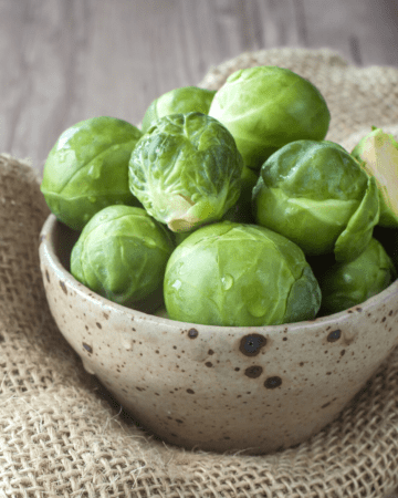 Brussels Sprouts in beige bowl sitting on burlap
