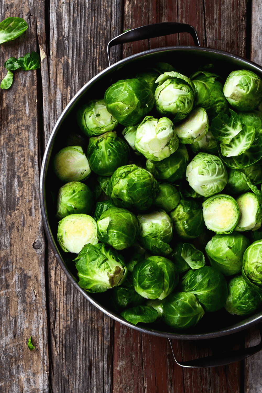 overhead view of Brussels Sprouts in silver bowl with wooden background