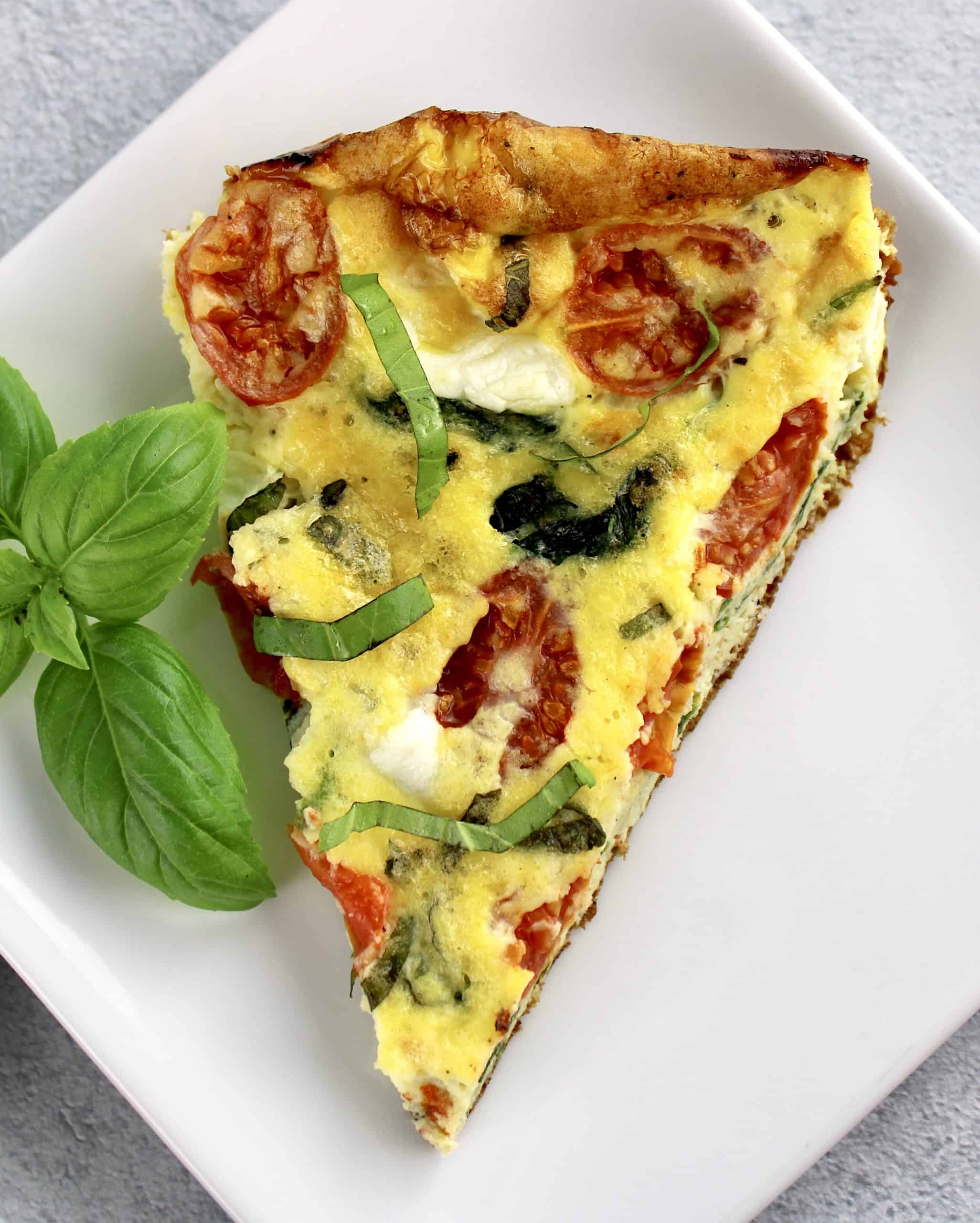 slice of caprese frittata on white plate with basil on side
