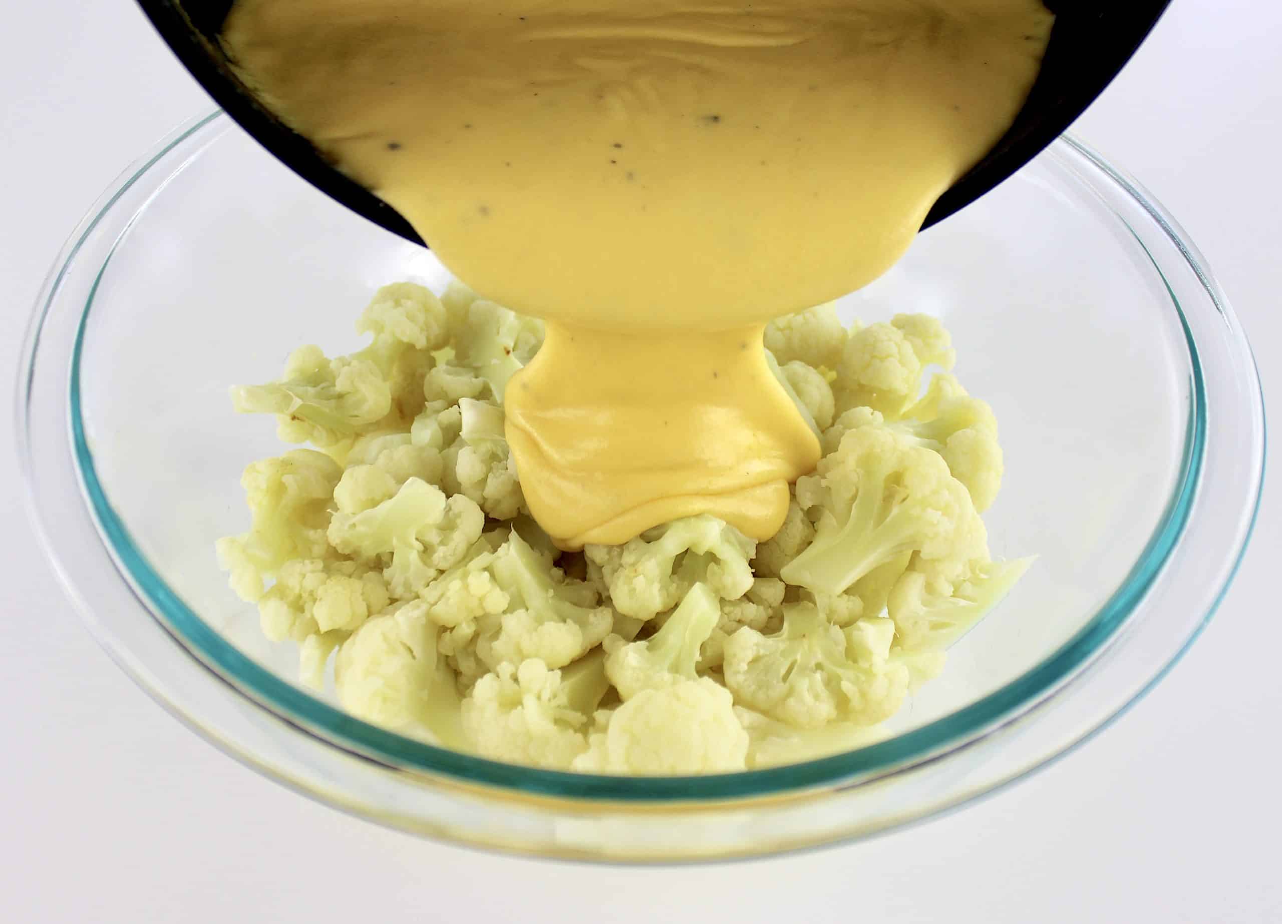 cheese sauce being poured over cooked cauliflower florets in glass bowl
