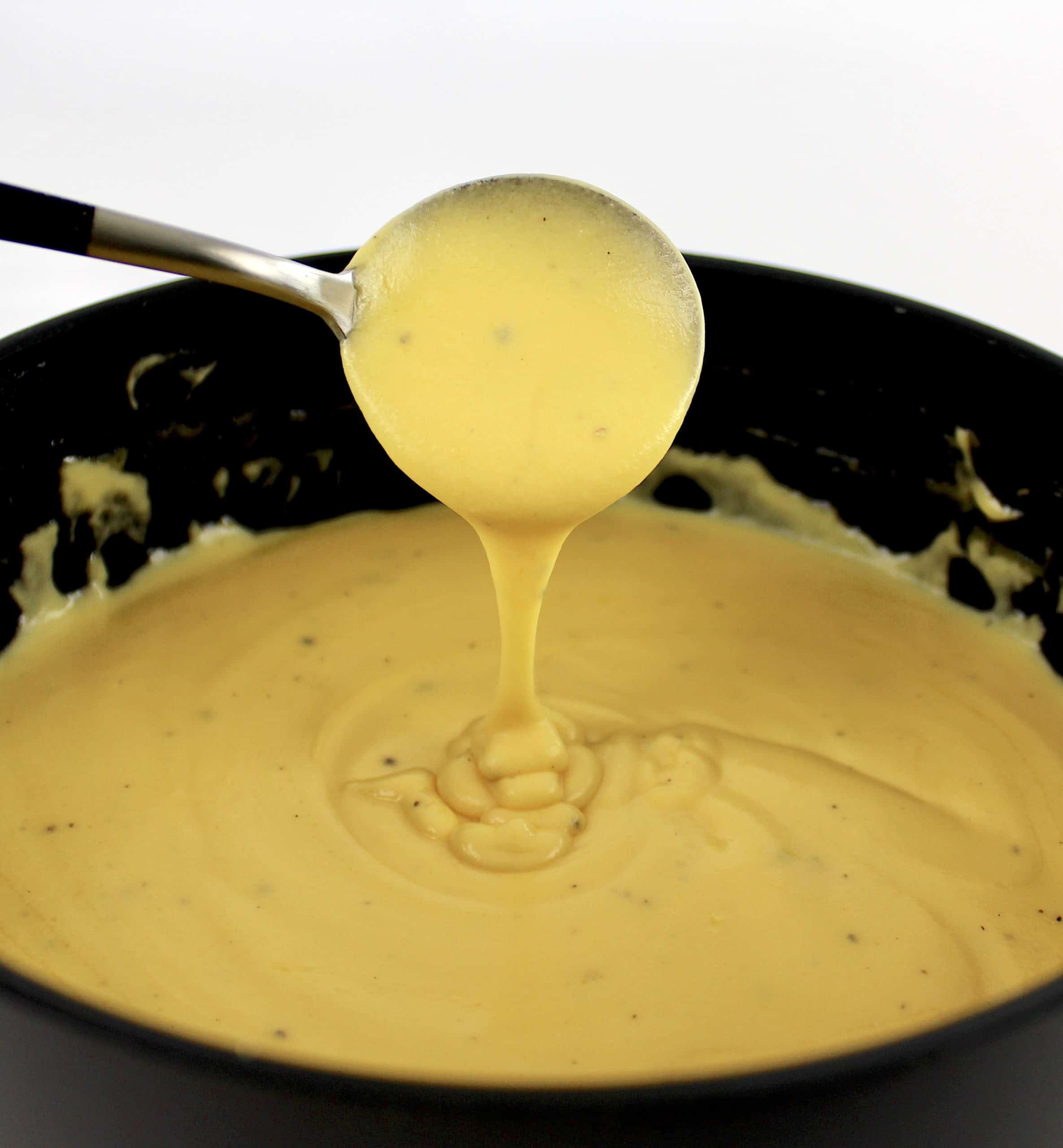 cauliflower mac and cheese sauce in saucepan being spooned