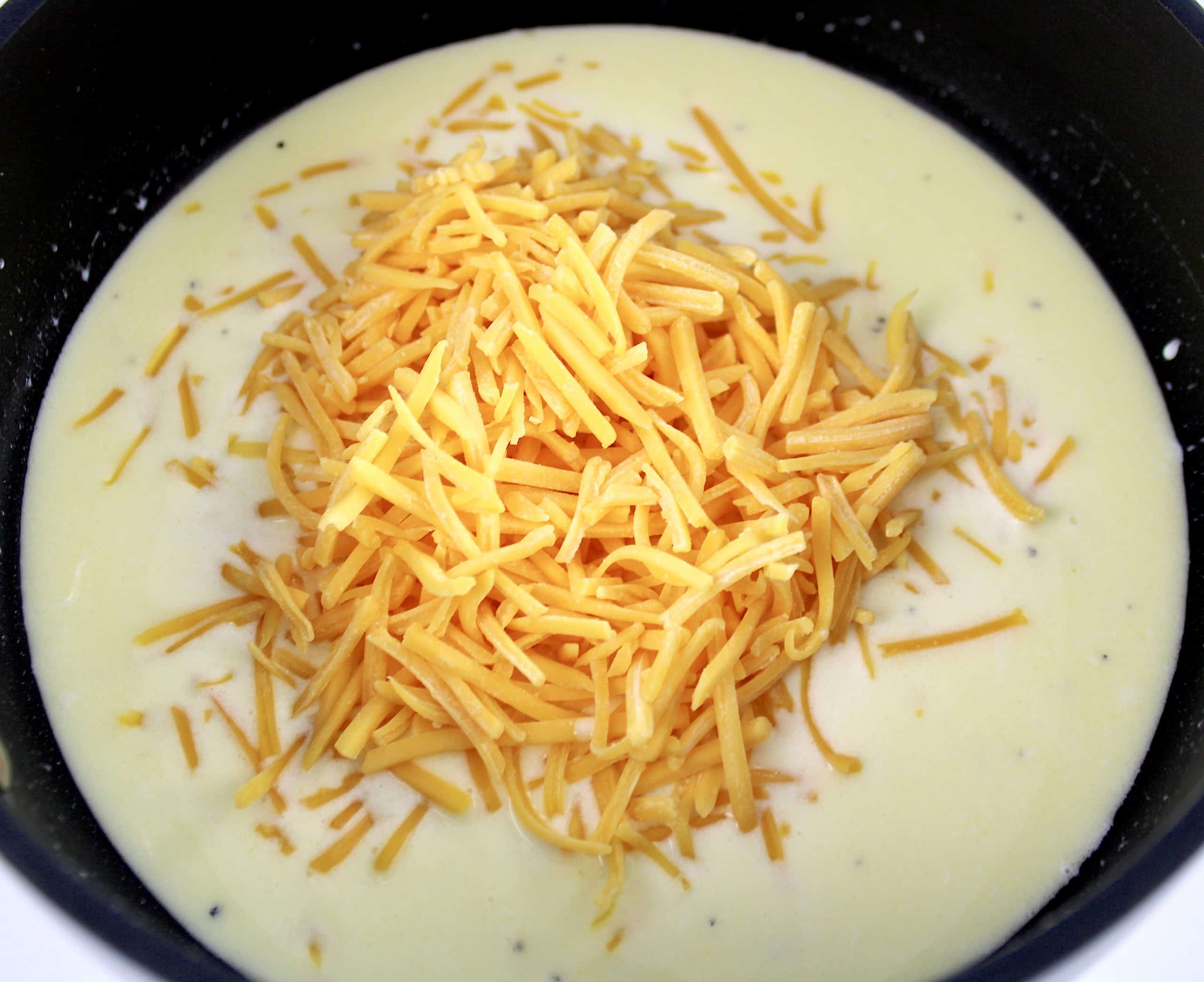cream sauce with shredded cheddar cheese on top in saucepan