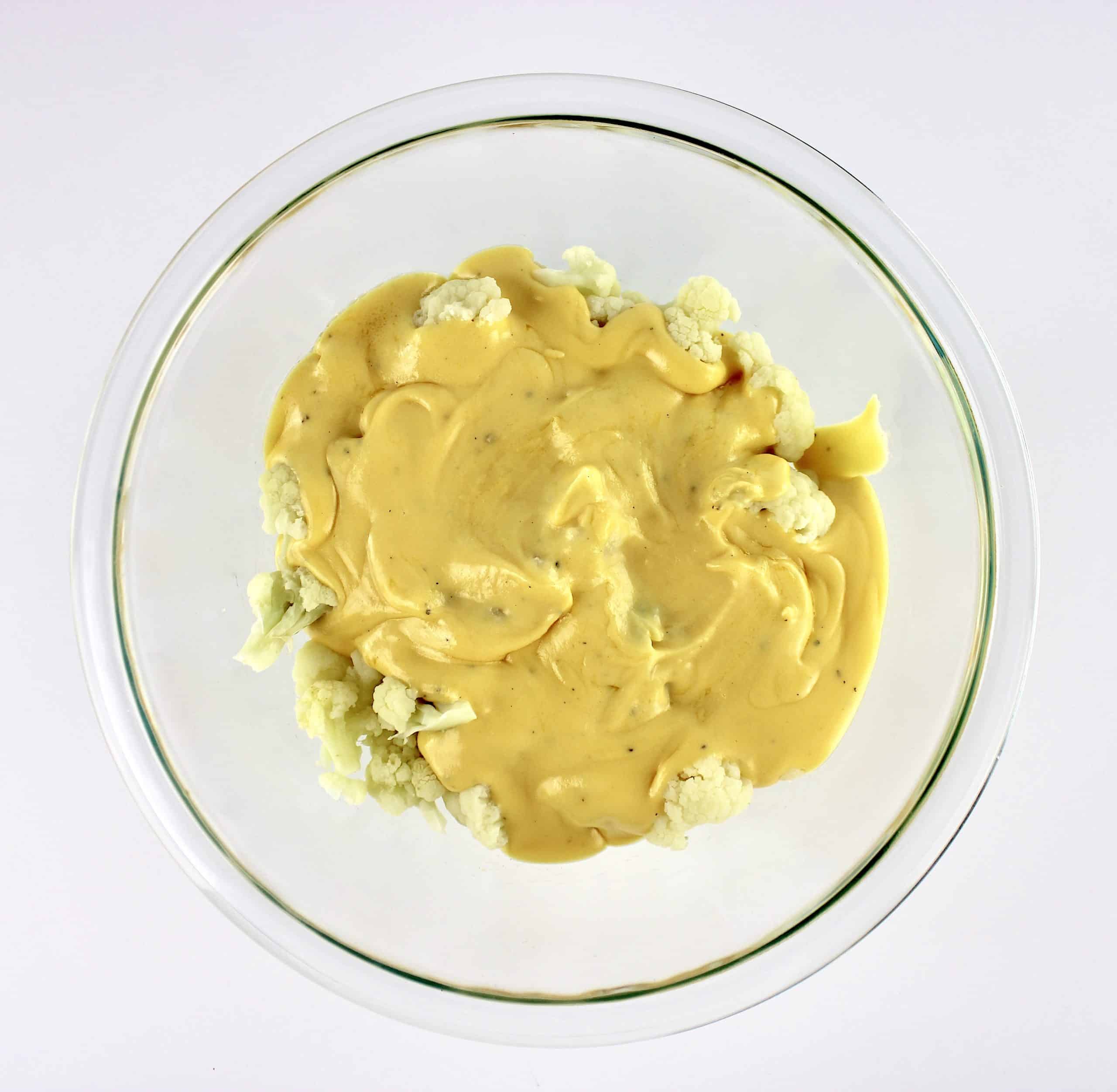 cheese sauce over the top of cauliflower florets in glass bowl