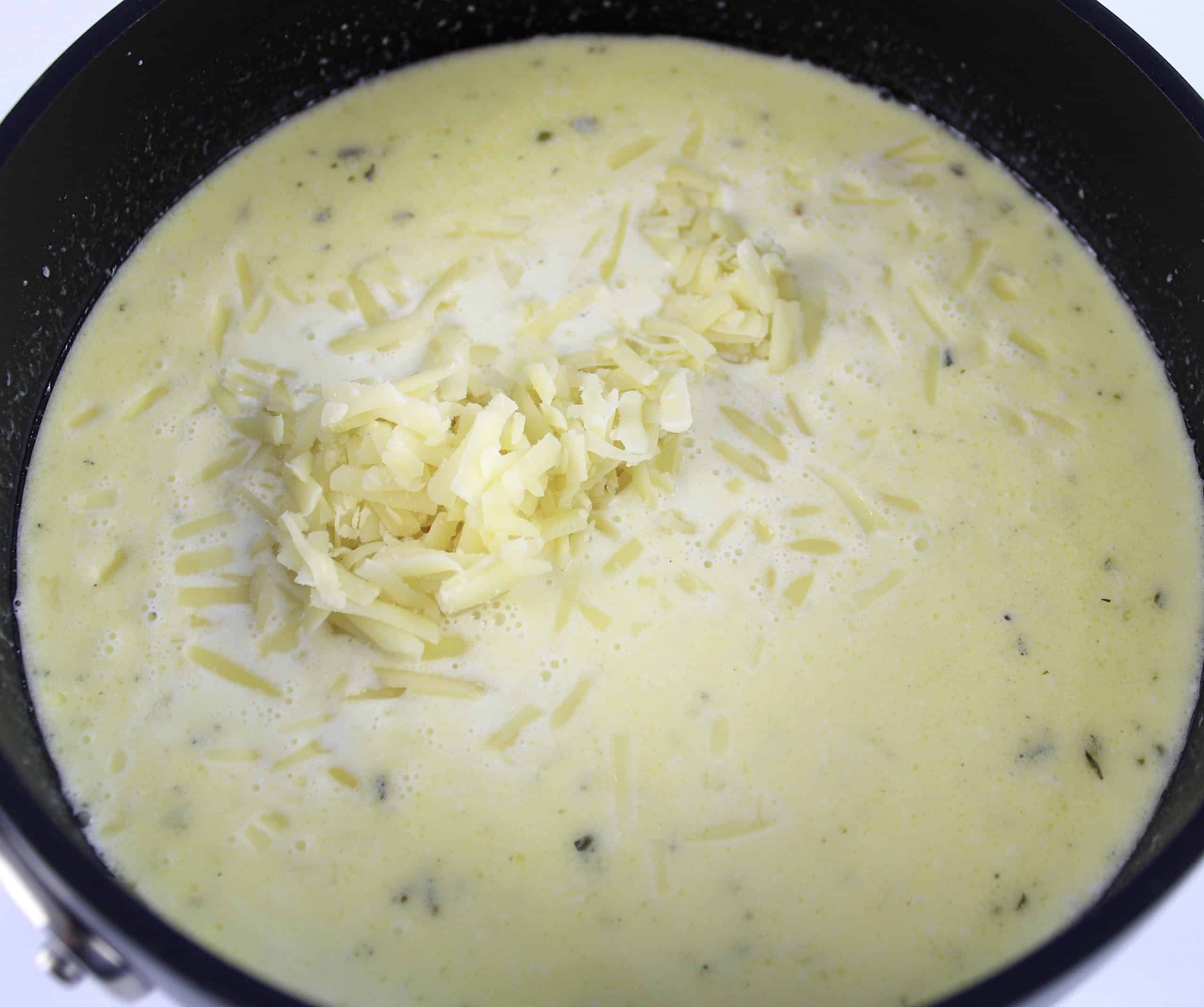 gruyere cheese sauce in saucepan with shredded cheese on top