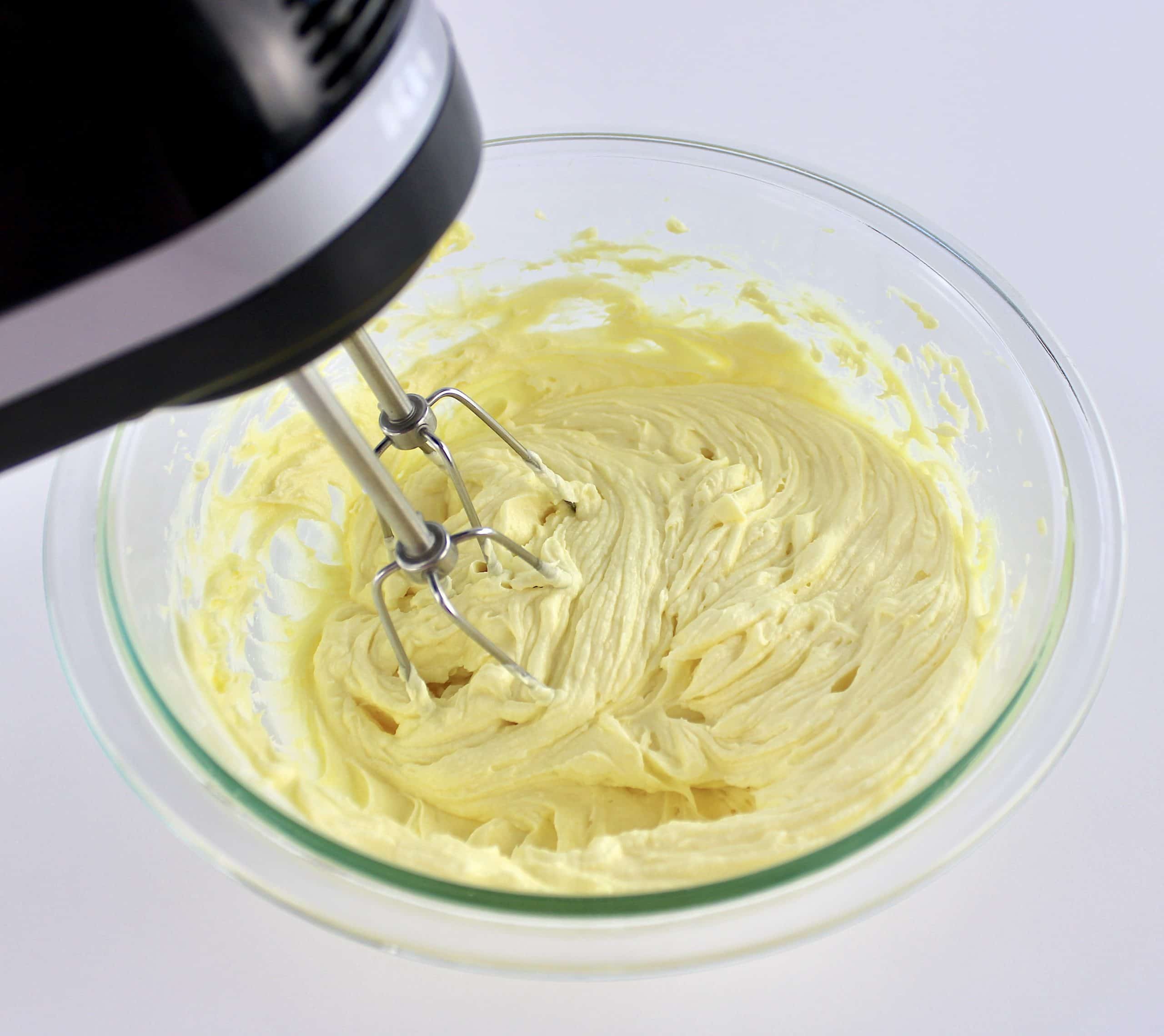 lemon frosting being mixed with hand mixer in glass bowl