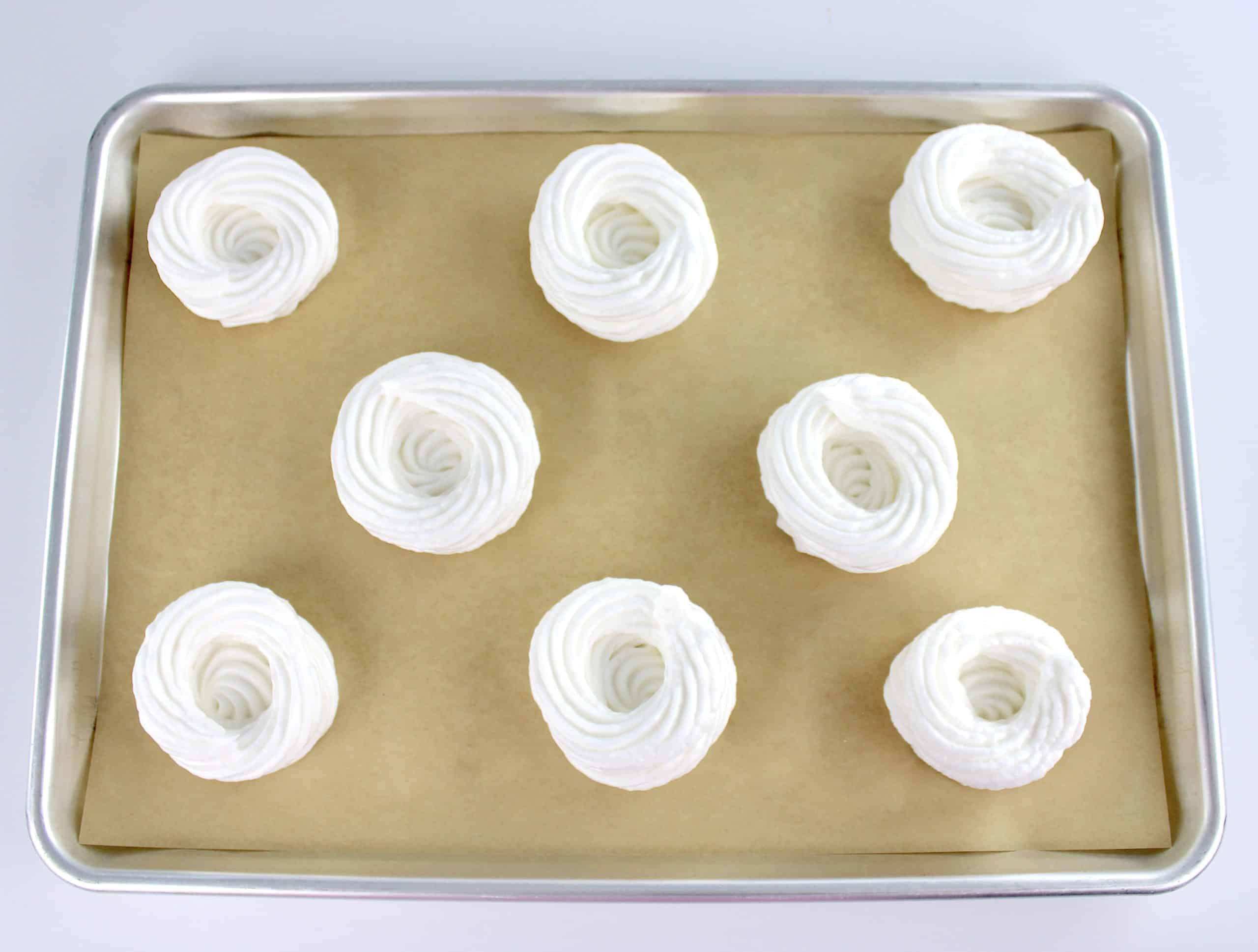 8 mini pavlovas unbaked on sheet pan lined with parchment paper