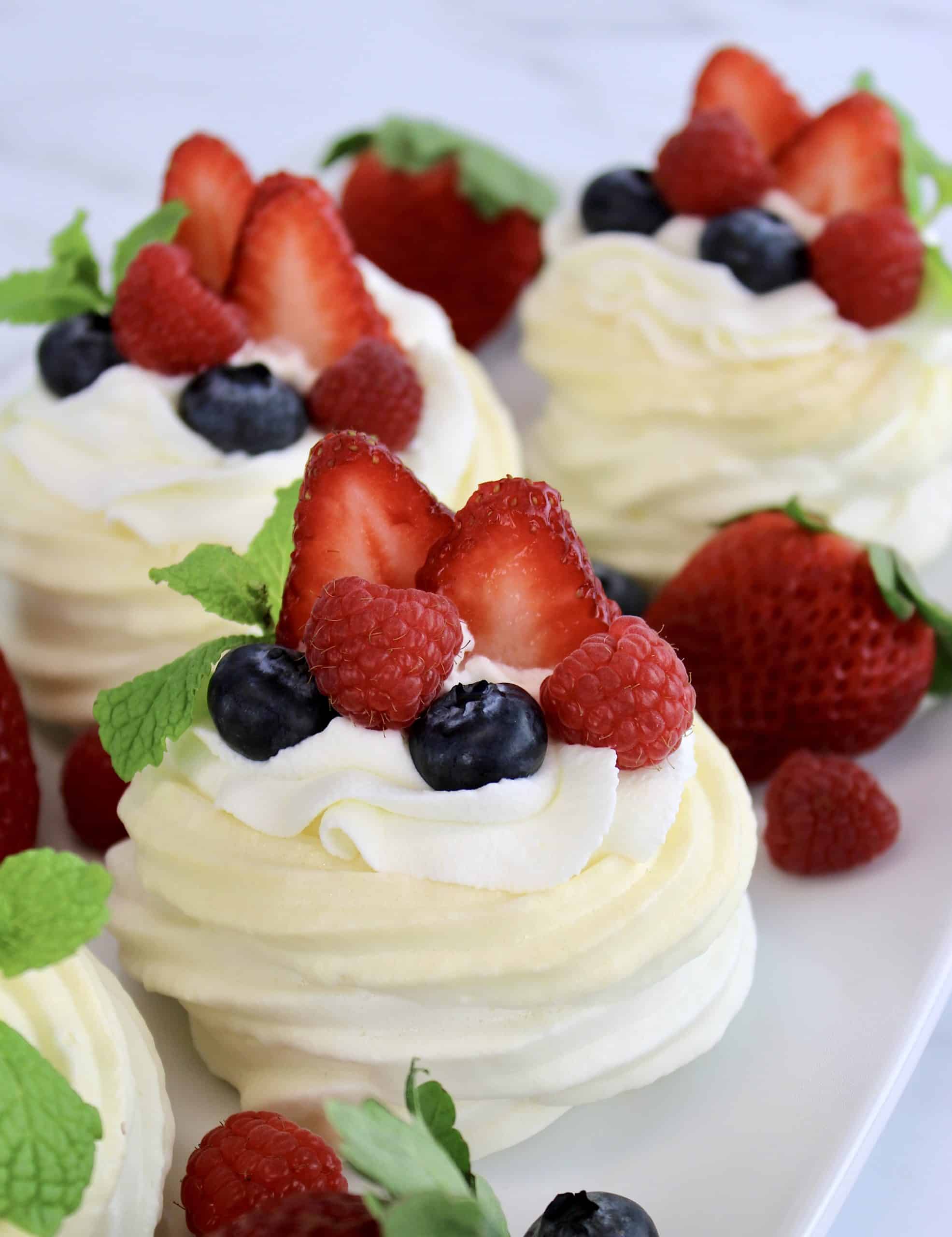 3 Mini Keto Pavlovas with whip cream and berries on top on white plate