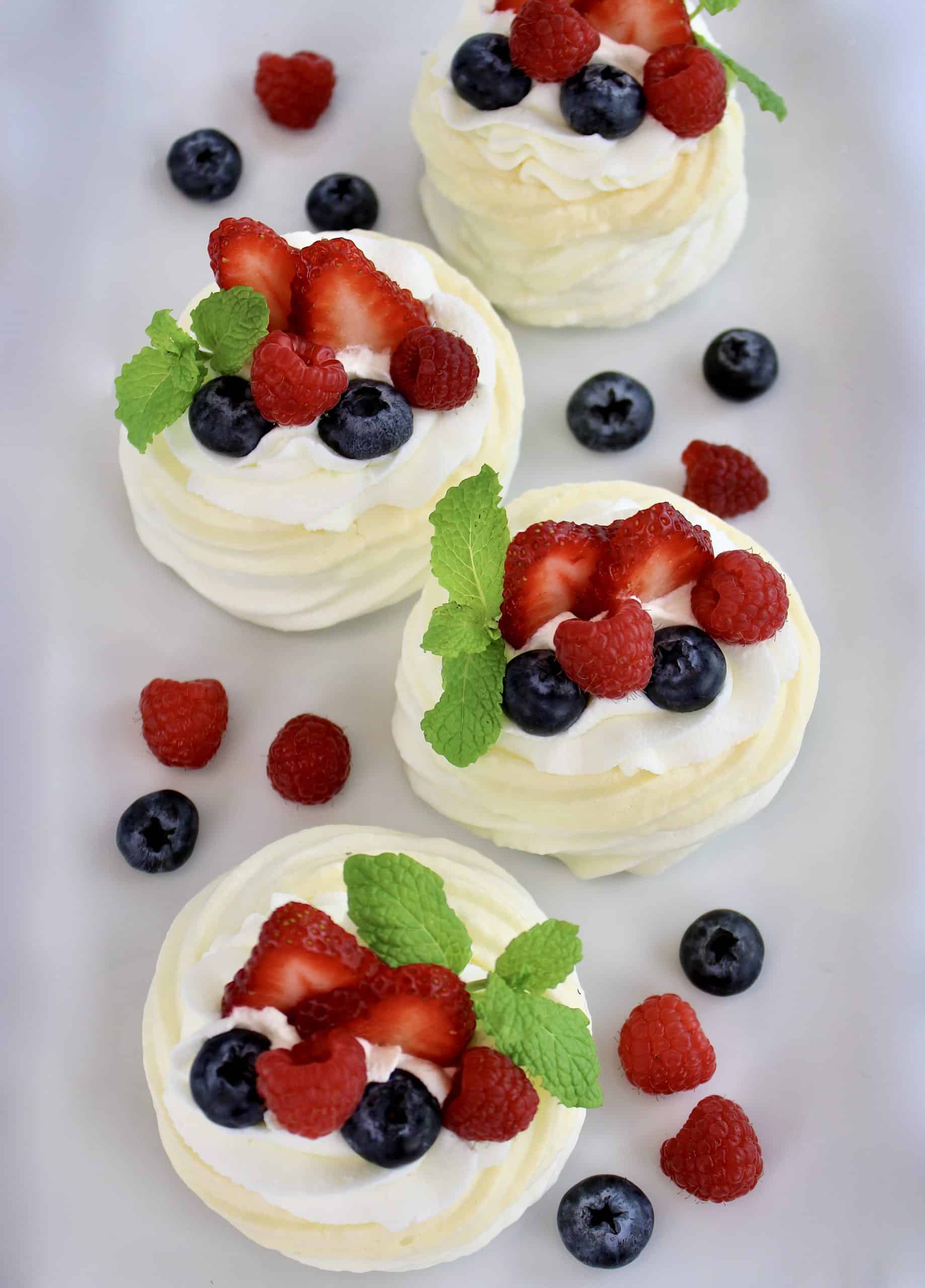 4 Mini Keto Pavlovas on white plate with berries around the plate and on top