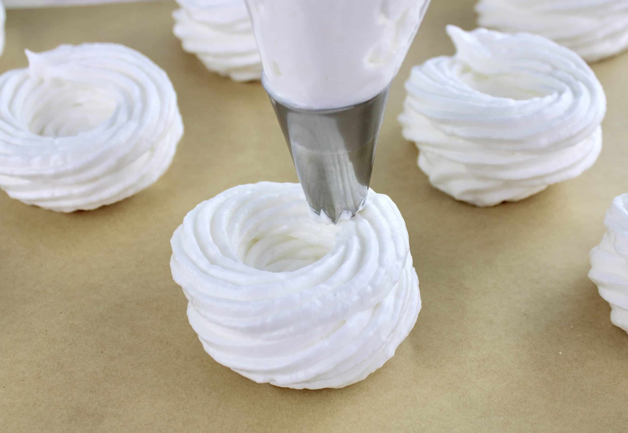 pavlovas being piped out onto parchment lined baking sheet