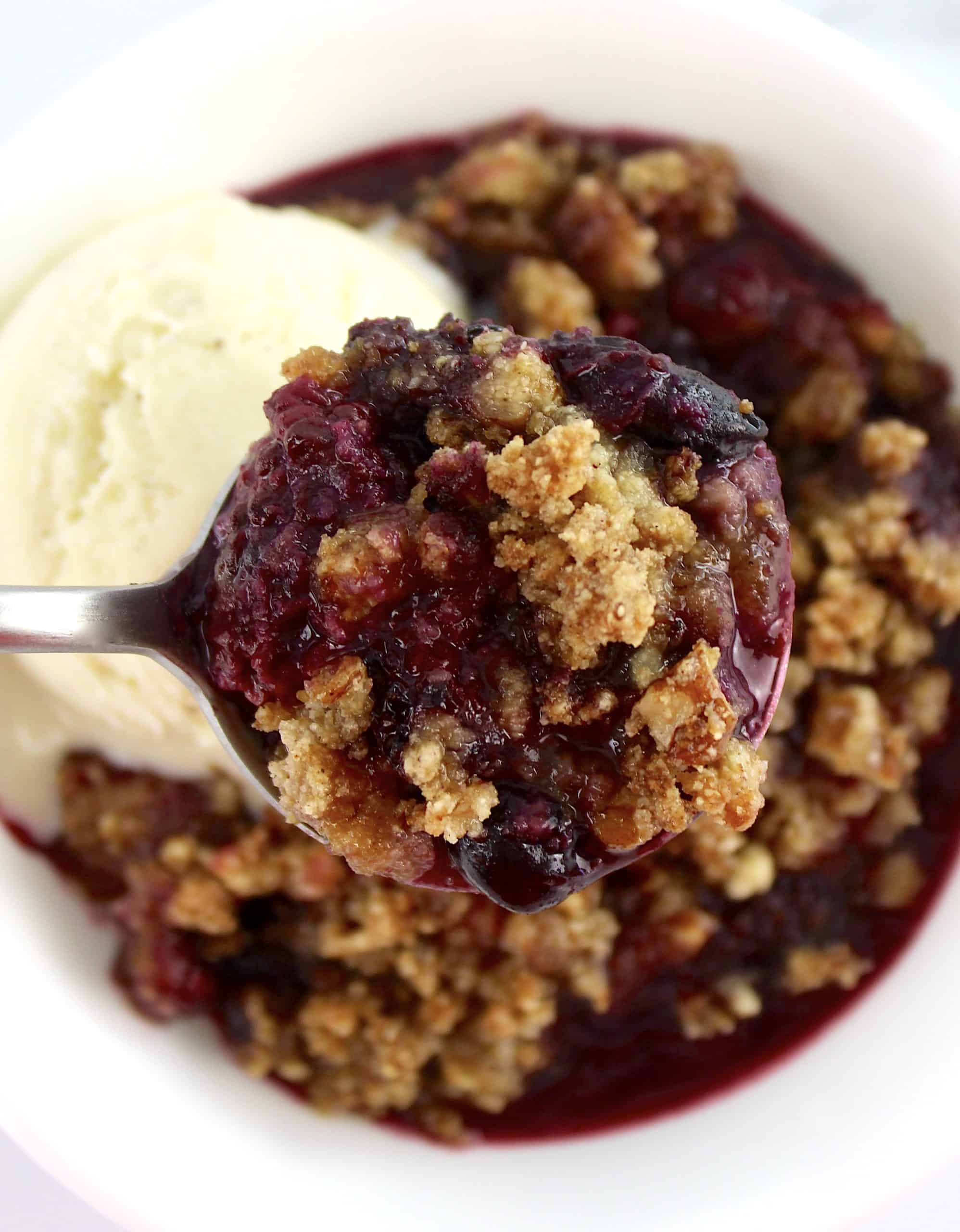 mixed berry crumble in spoon over crumble in white bowl