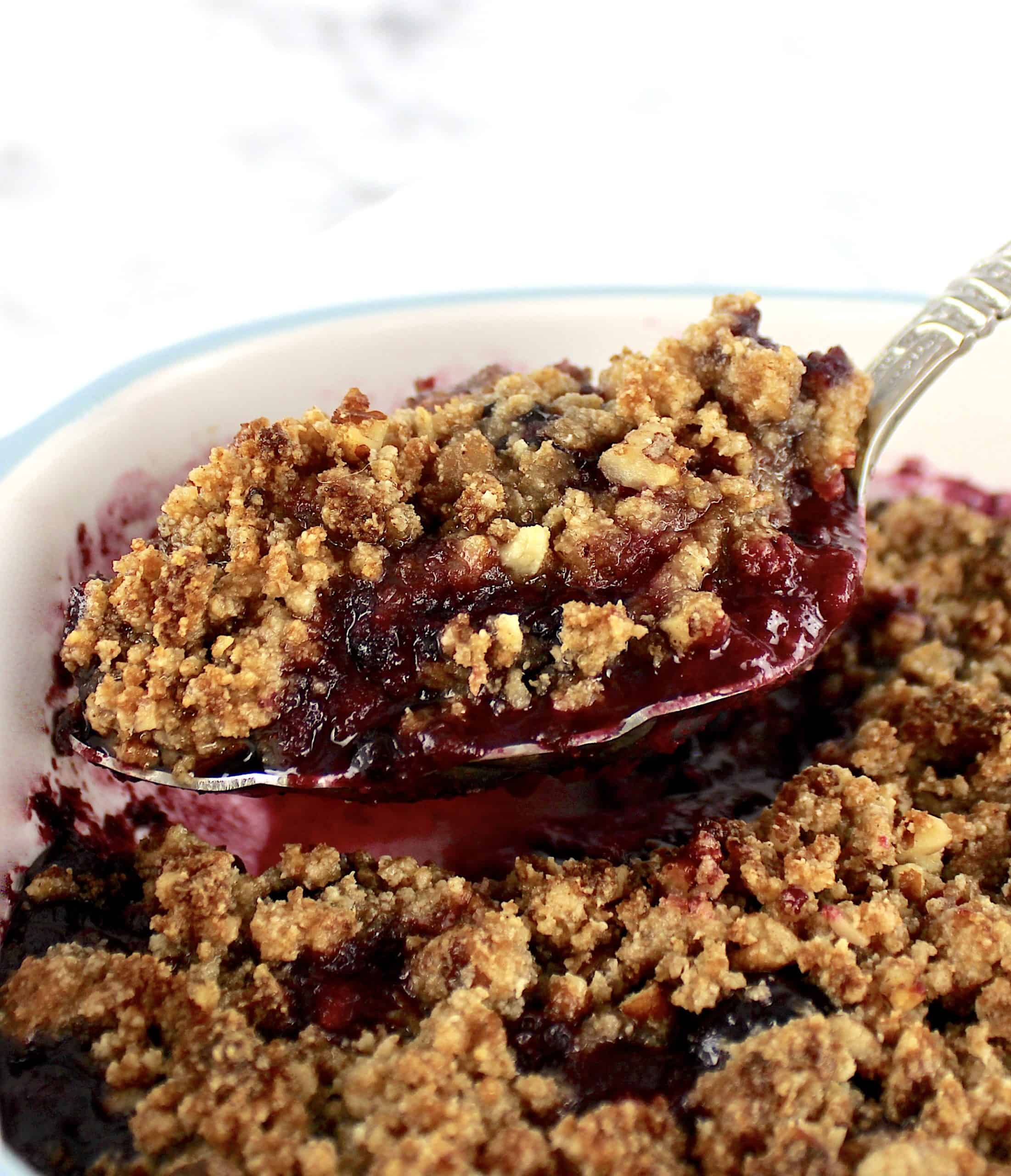 closeup of mixed berry crumble in casserole being scooped out