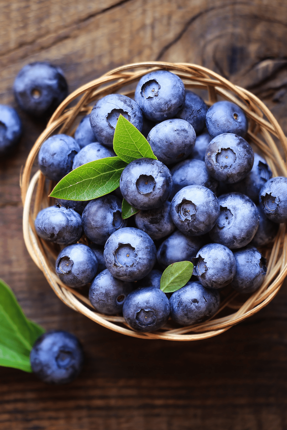 overhead view of blueberries in brown basket with wooden background