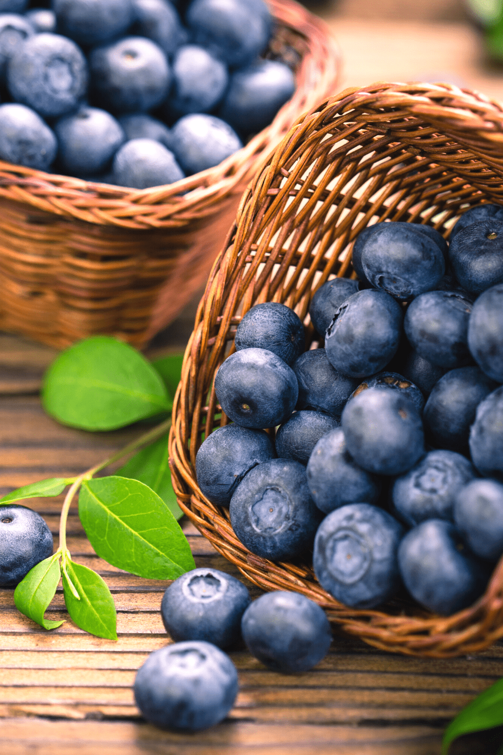 Blueberries spilling out of brown basket onto wooden board