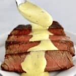 Béarnaise Sauce being spooned over sliced steak on white plate