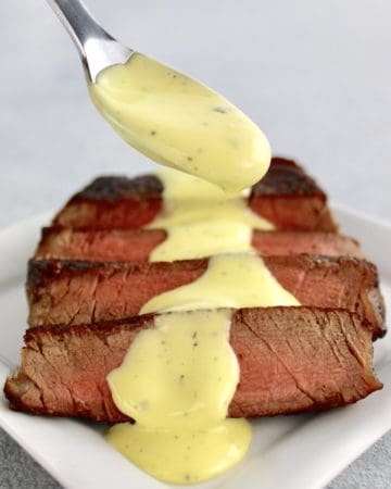 Béarnaise Sauce being spooned over sliced steak on white plate