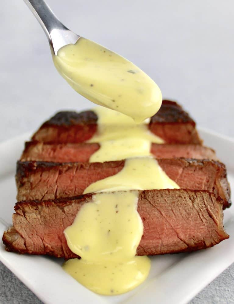 Béarnaise Sauce being spooned over sliced steak on white plate