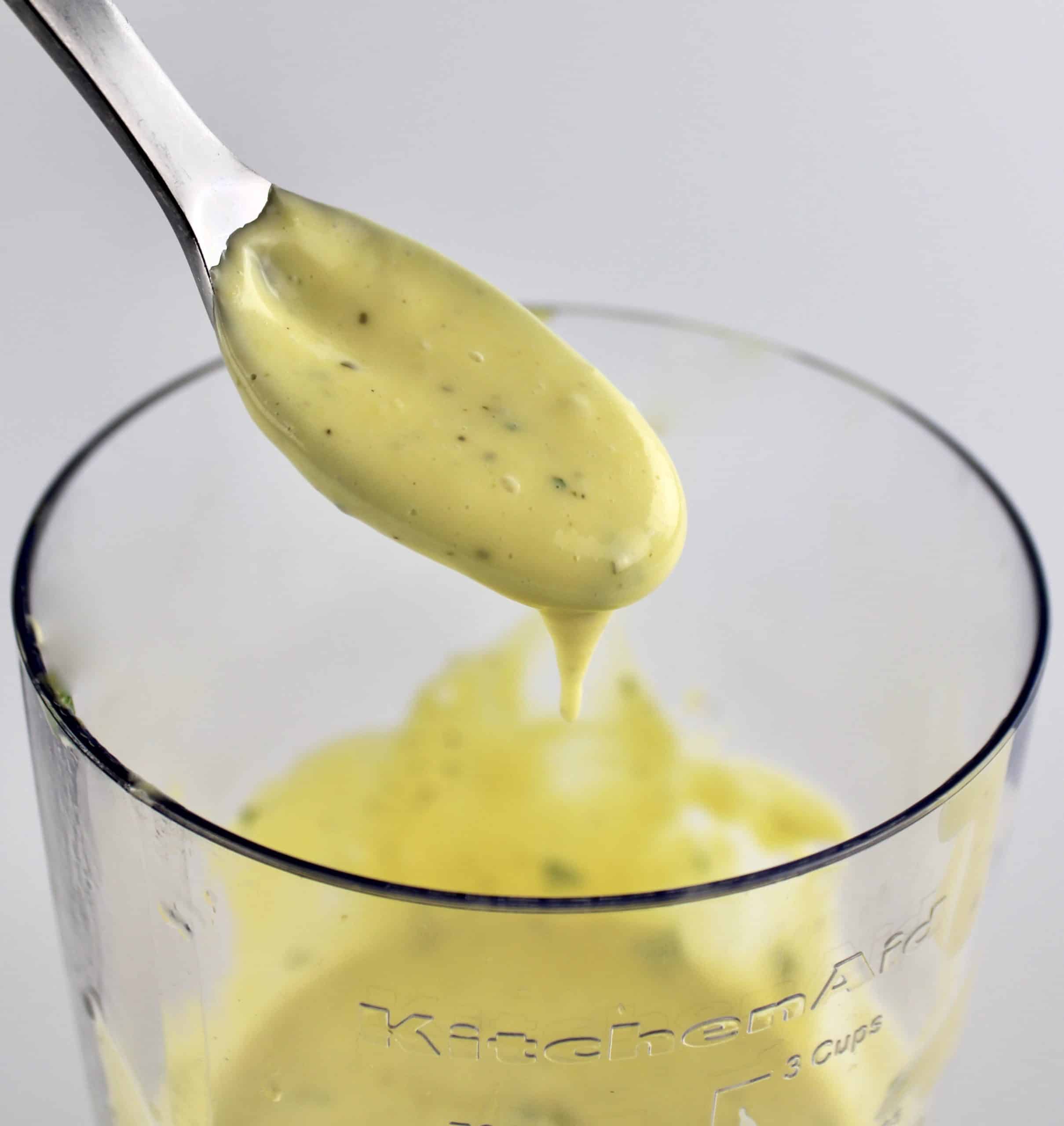 Béarnaise sauce dripping off spoon over immersion blender cup
