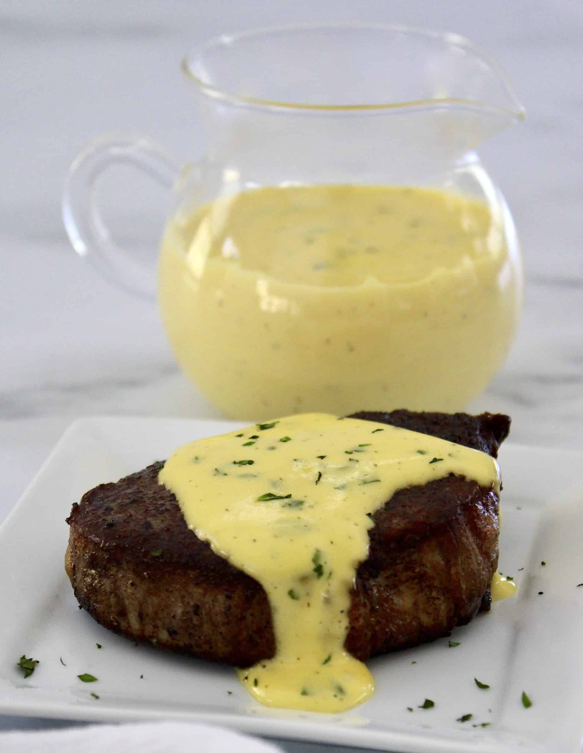 filet mignon on white plate with béarnaise sauce on top and in background