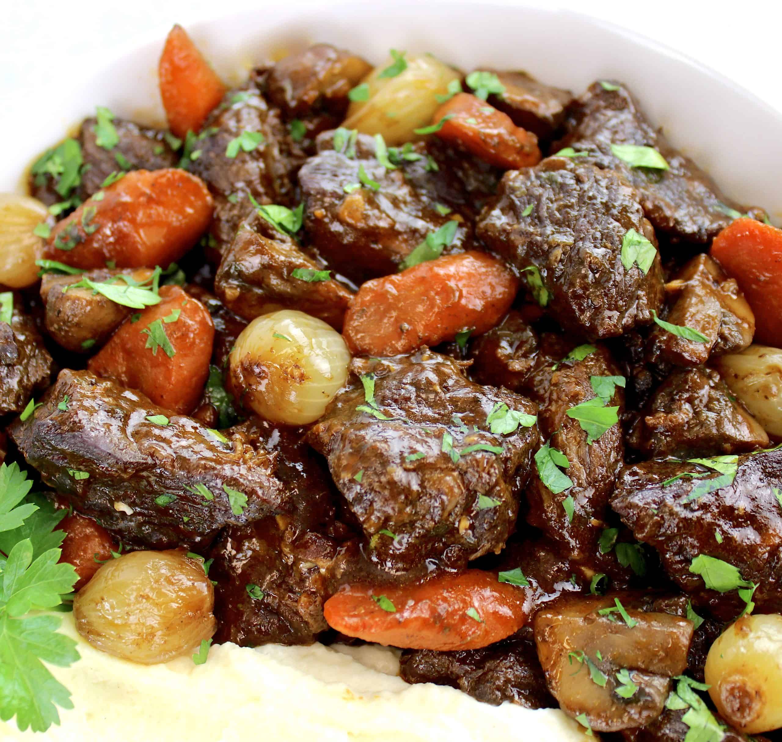 closeup of Beef Bourguignon in white bowl with mashed cauliflower and parsley garnish