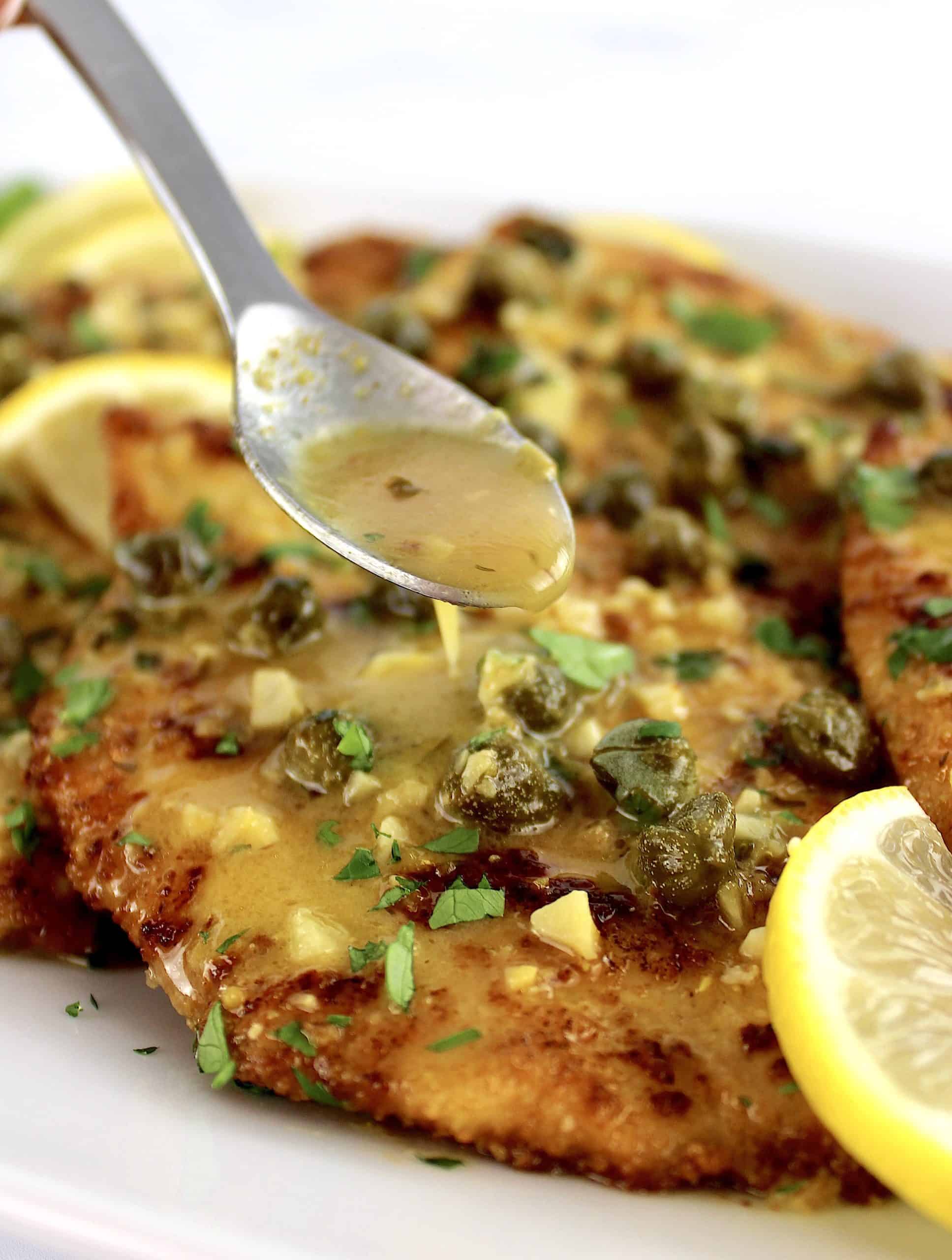 Chicken Piccata with sauce being spooned over top and lemon slices on side