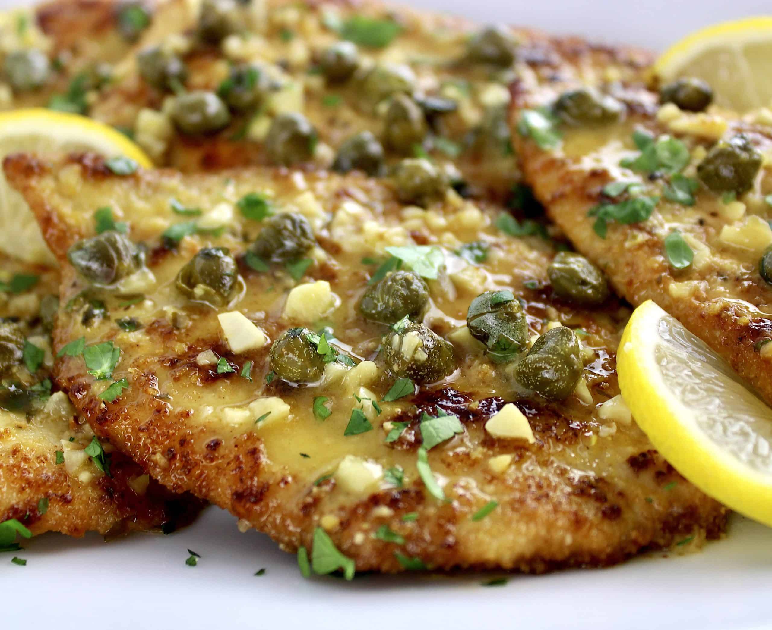 closeup of piece of Chicken Piccata on white plate with capers on top
