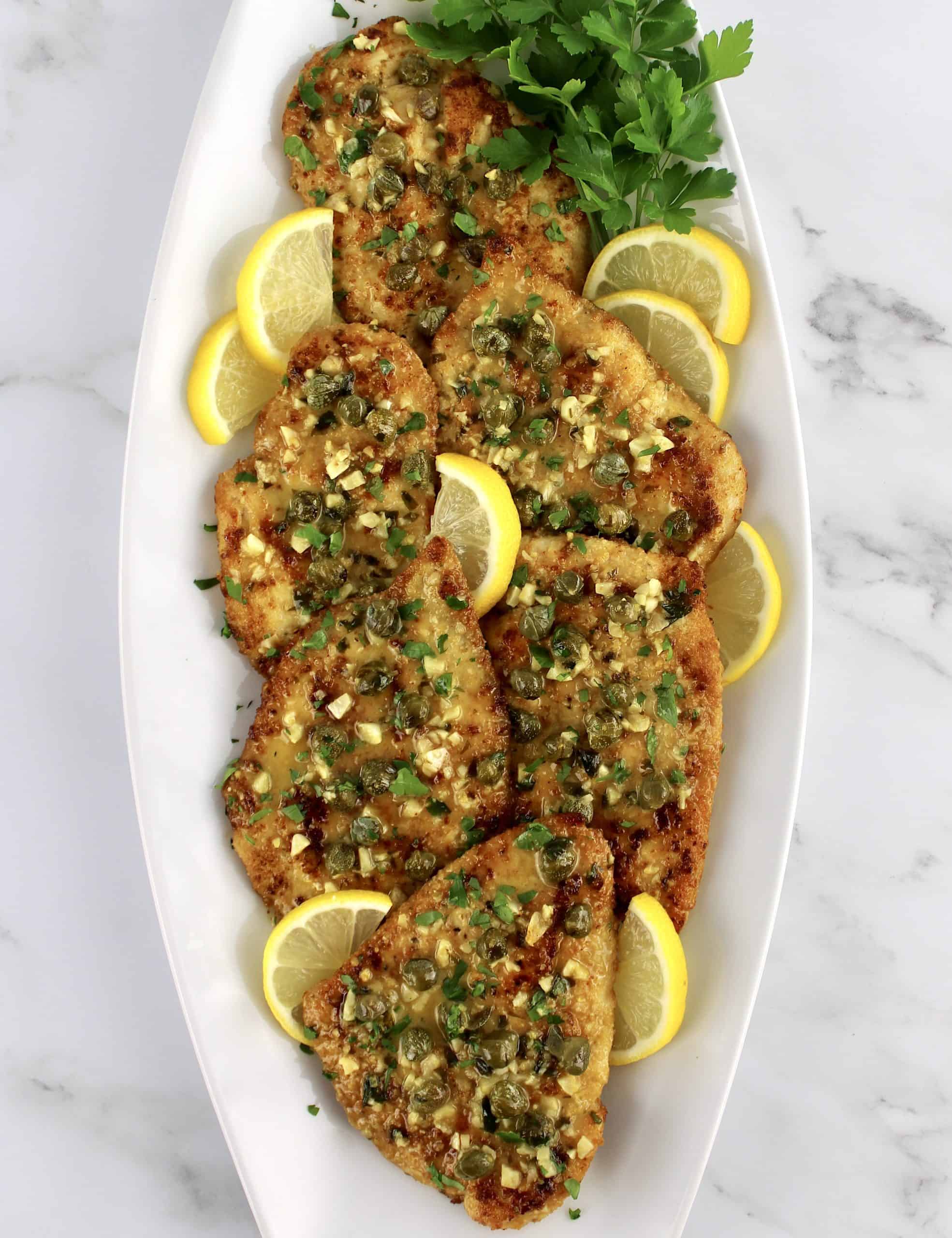 overhead view of Chicken Piccata on white plate with lemon slices and parsley