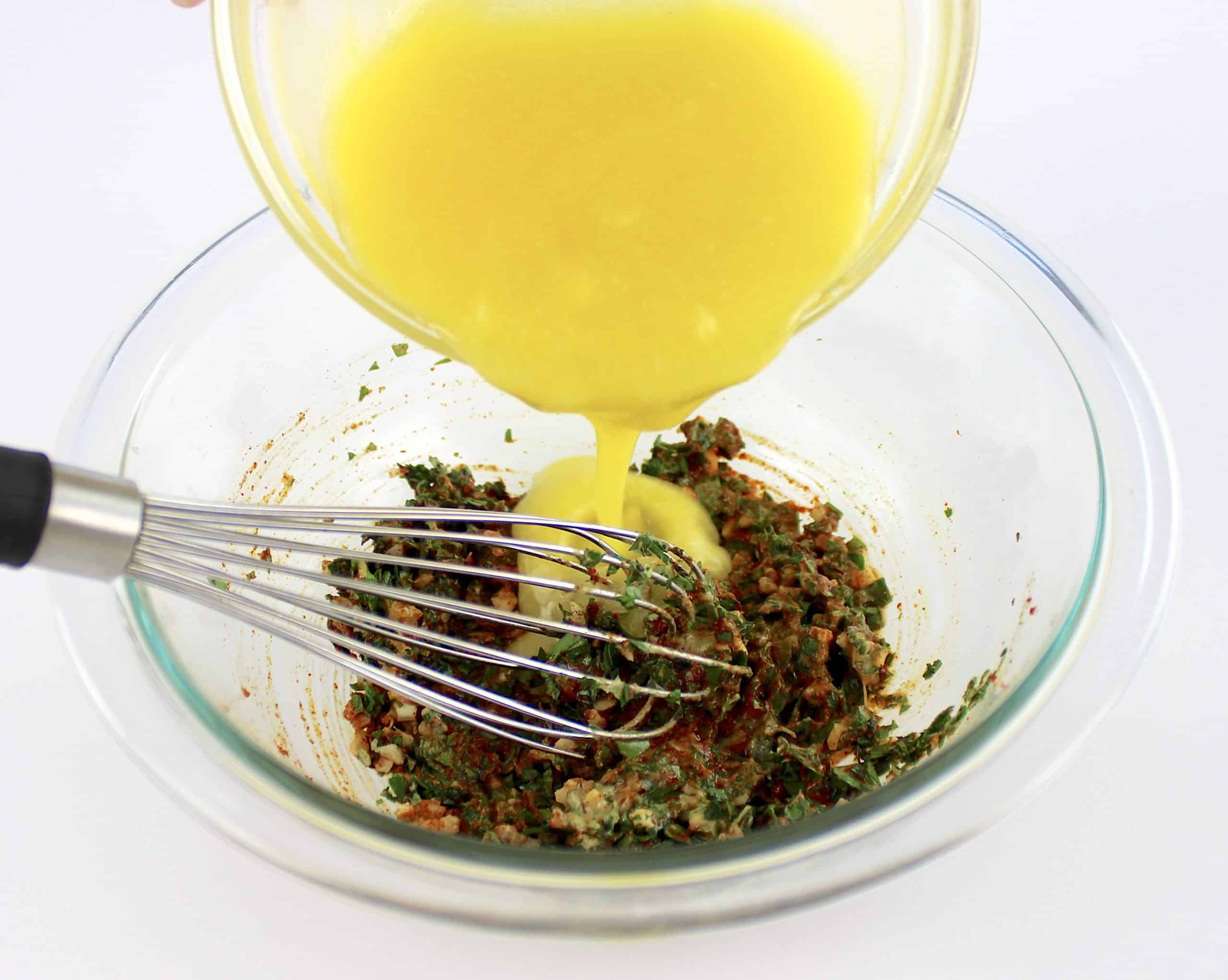 melted butter being poured into glass bowl with herbs and spices with whisk