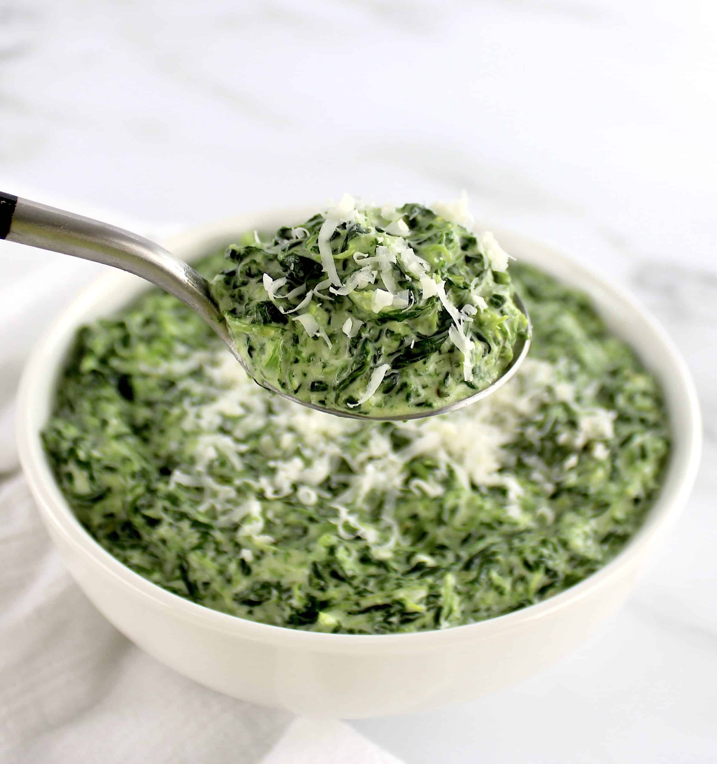 spoonful of creamed spinach with grated cheese on top held up over bowl