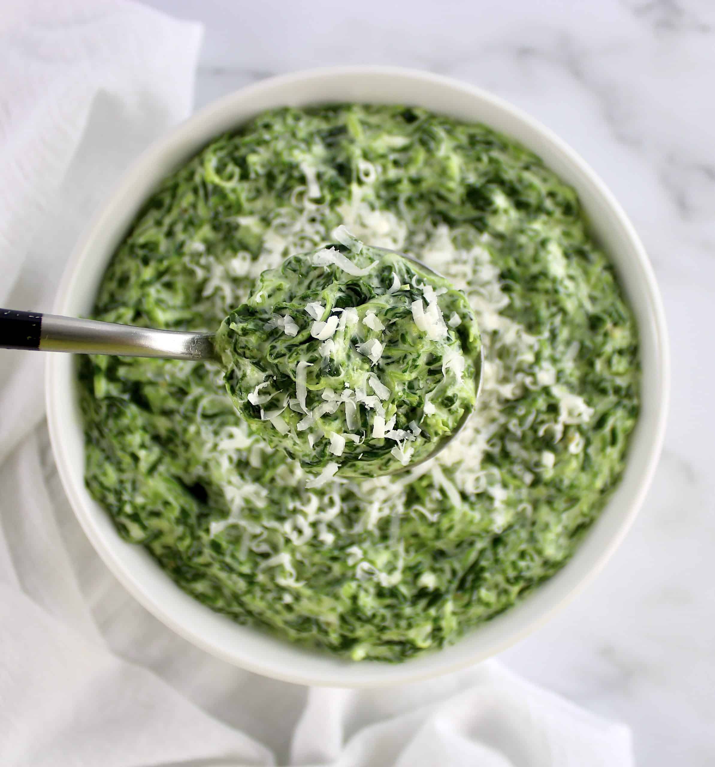 spoonful of creamed spinach with grated cheese on top held up over bowl