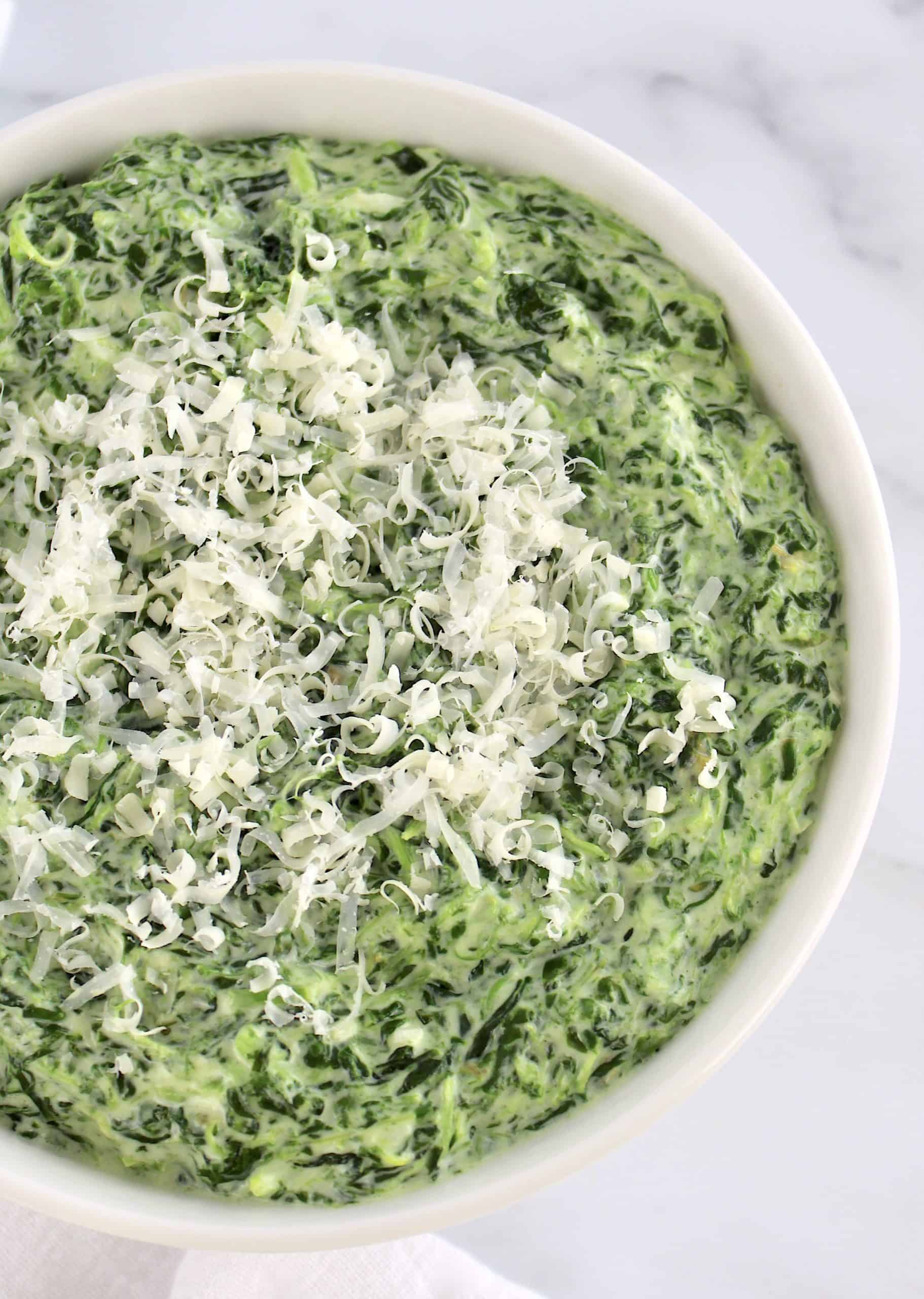 creamed spinach in white bowl with grated cheese on top