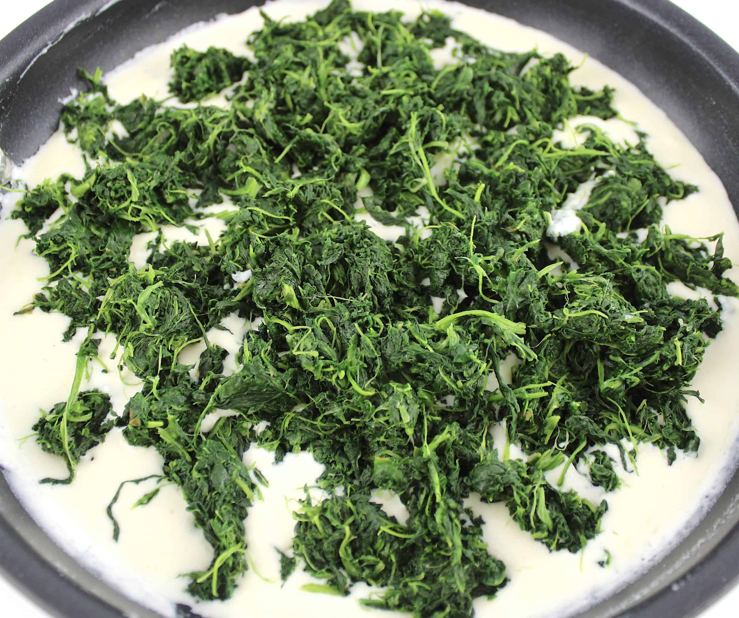 cooked spinach in skillet sitting on cream sauce unmixed