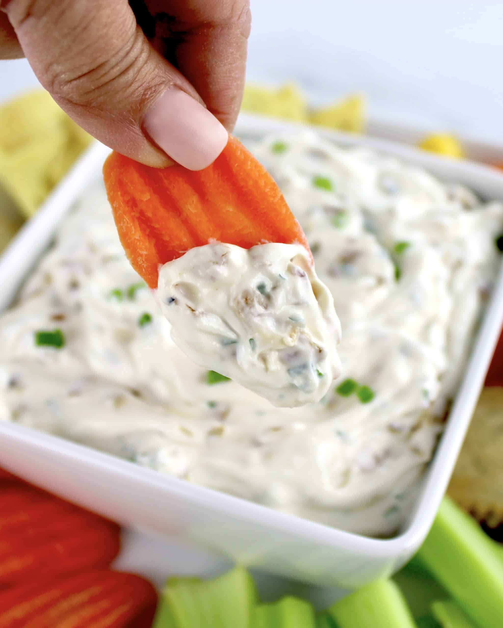 carrot being dipped into Homemade French Onion Dip in white bowl